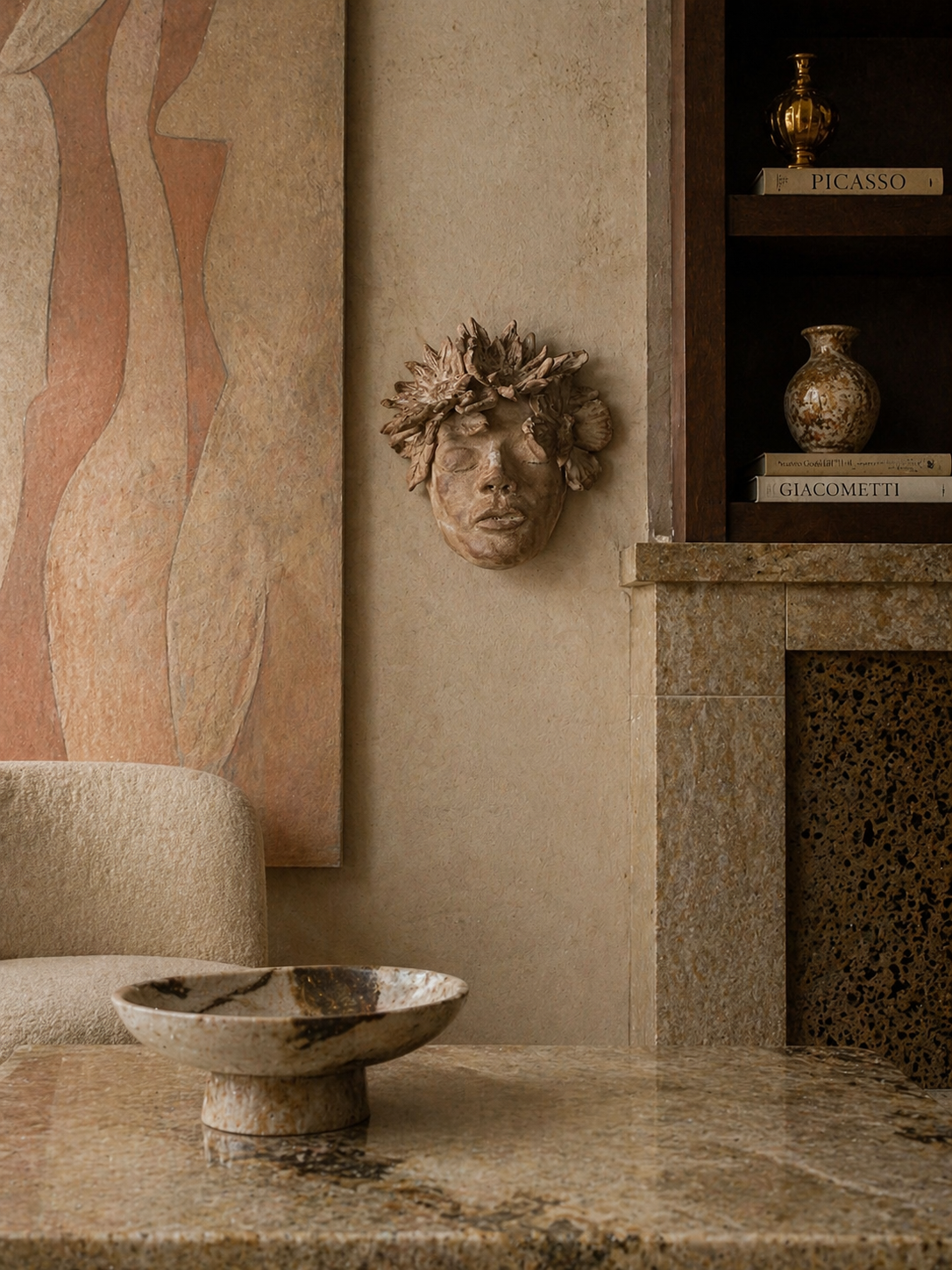 Décor intérieur avec sculpture de visage féminin en terre cuite avec des fleurs dans les cheveux, étagère avec livres et vases en céramique, table en pierre avec bol en marbre.