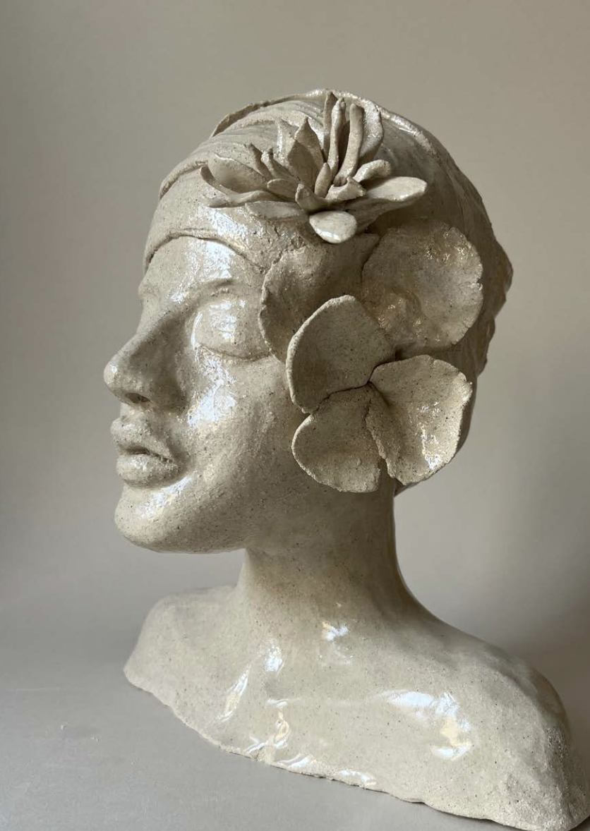 Une sculpture en pierre d'une tête de femme avec des fleurs intégrées dans ses cheveux, vue de profil.