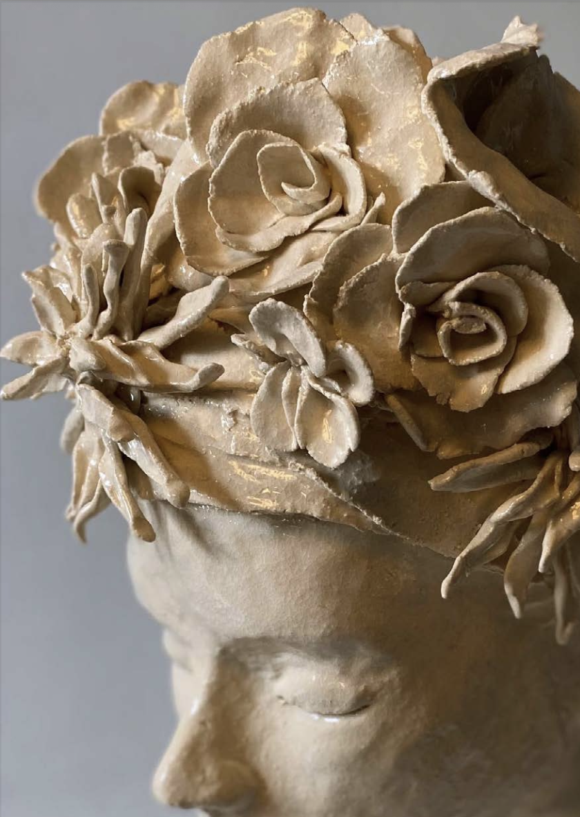 Statue en céramique ou en pierre représentant une tête avec des fleurs sculptées en relief sur la tête.