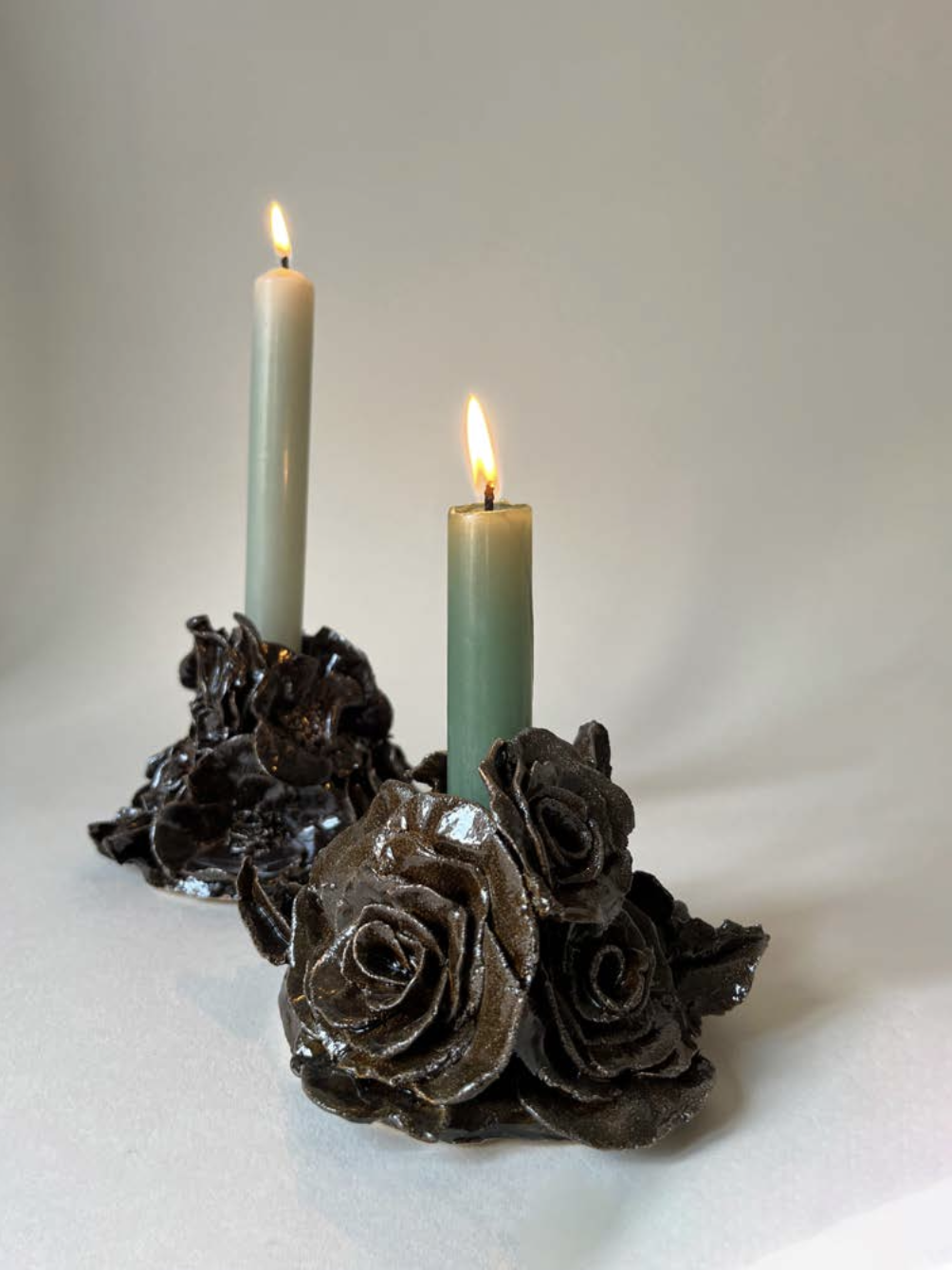 Deux bougies allumées, entourées de décorations en forme de roses en métal noir.