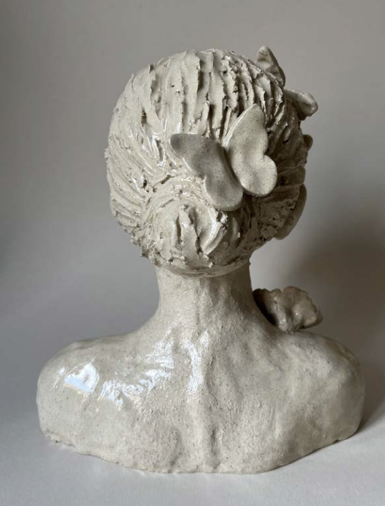 Sculpture en céramique d'une tête de femme avec des cheveux bouclés, un papillon sur le visage et un petit animal, peut-être un chien ou un chat, sur l'épaule droite.