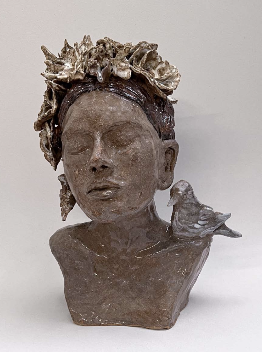 Une sculpture représentant une femme avec les yeux fermés, portant une couronne de fleurs sur la tête, accompagnée d'une colombe posé sur son épaule.