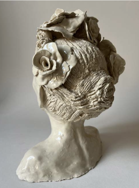 Sculpture en céramique représentant une tête humaine avec des détails floraux en haut.