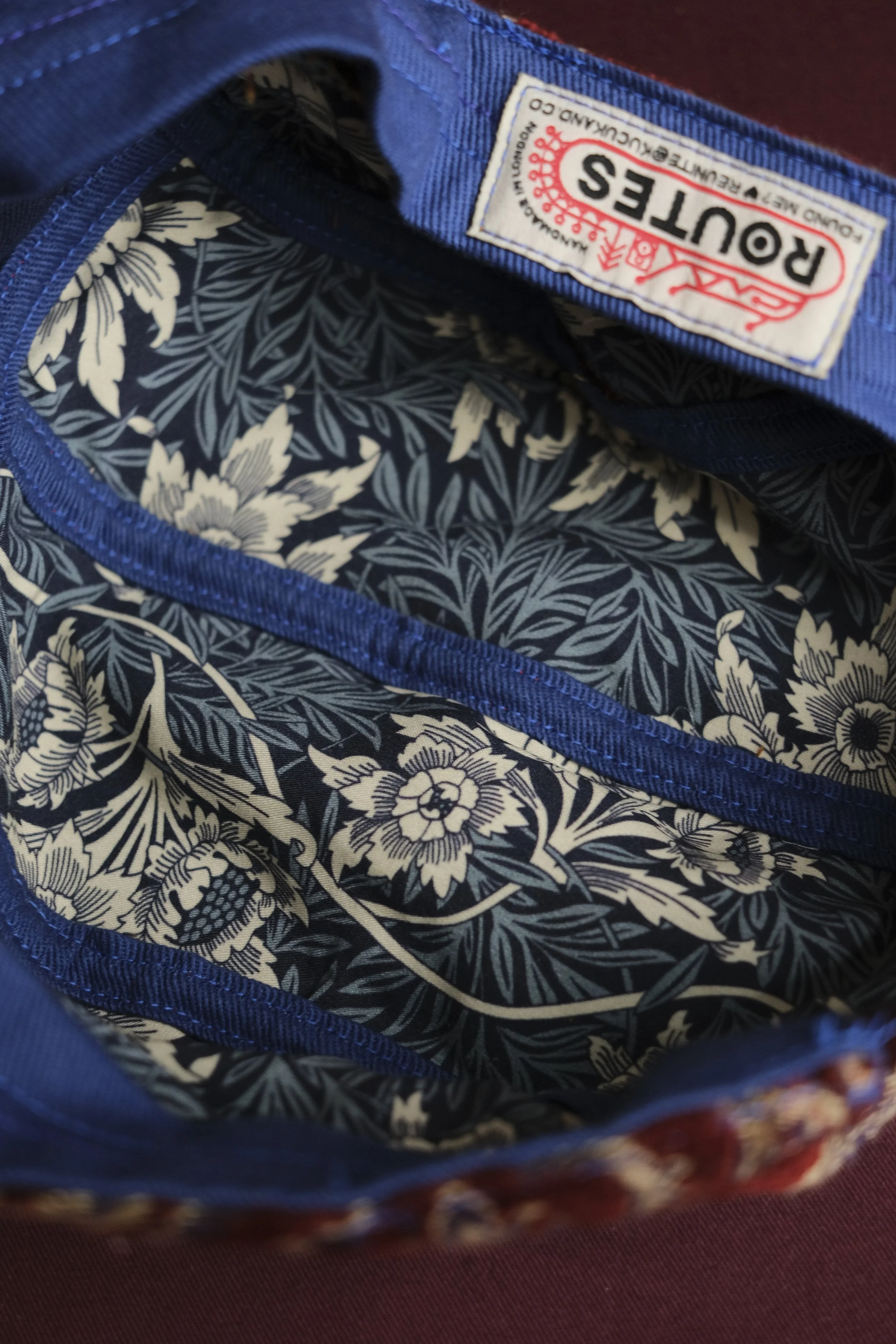 The image shows the inside of a blue fabric bag with a floral-patterned lining in black and white. The bag has a label that reads "ROUTES" with additional text indicating it is made in Europe.