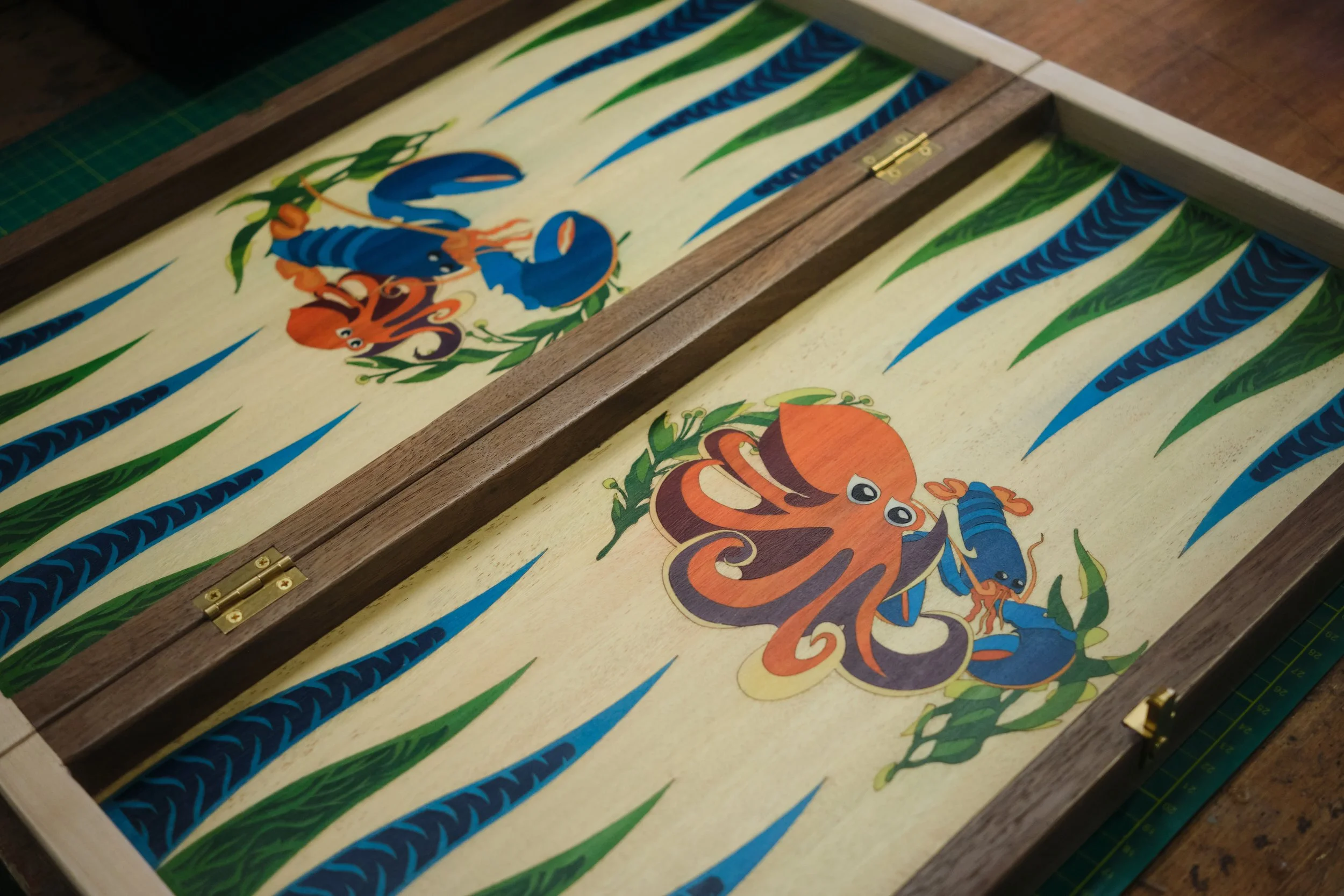 A colorful painted wooden box with a hinged lid, decorated with images of blue and orange lobsters and green underwater plants.