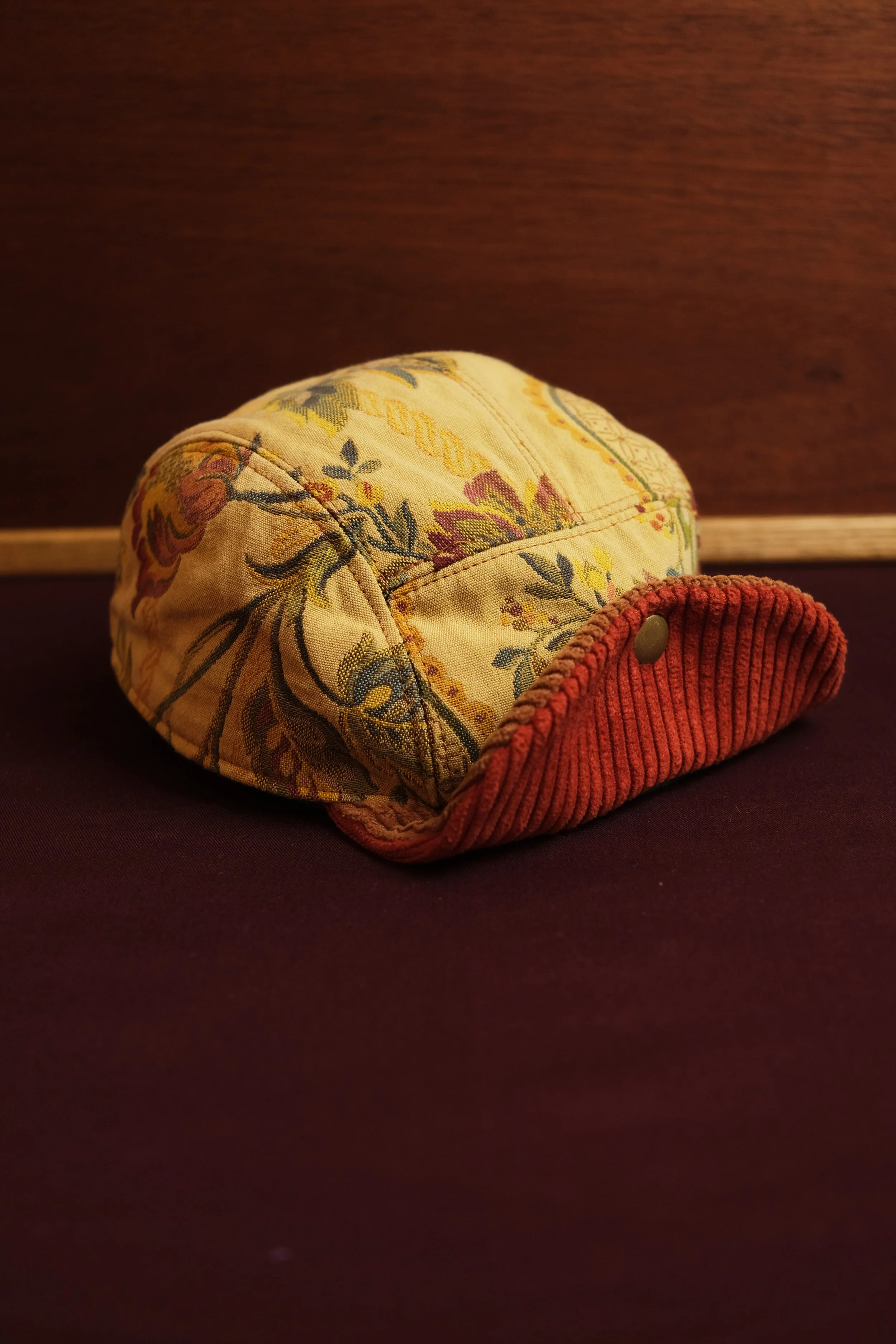 Close-up of a fabric hat with floral pattern and a red corduroy brim.