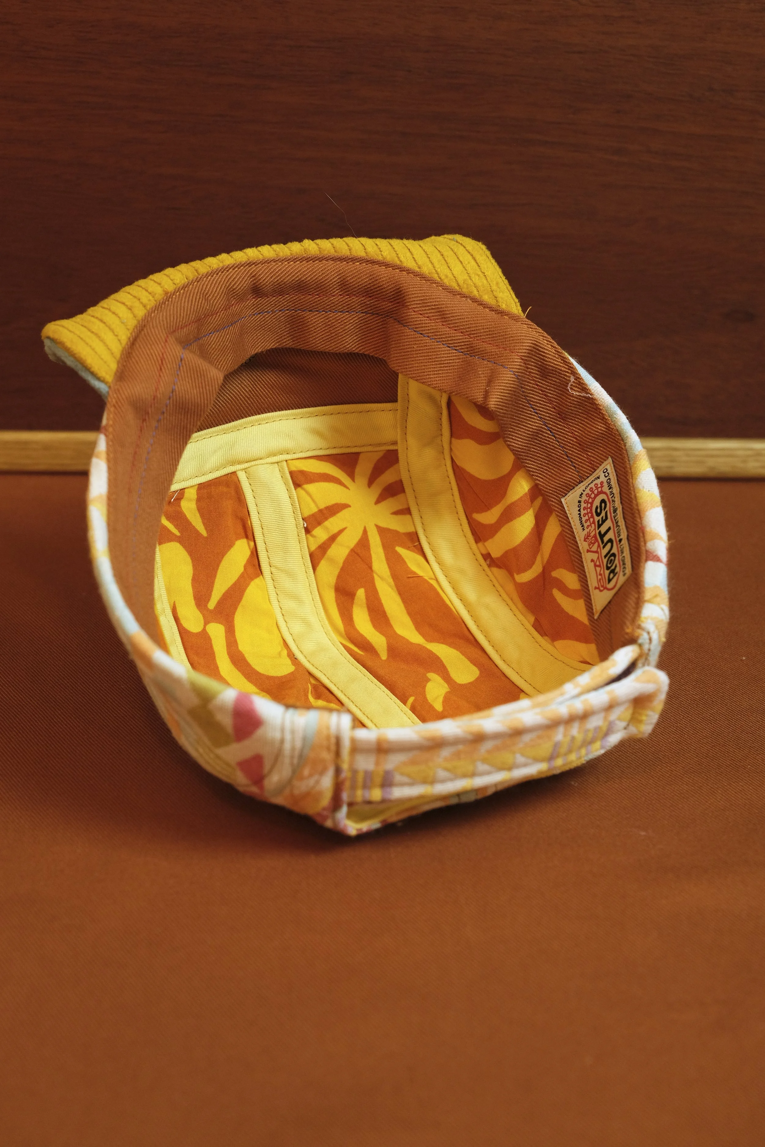 top view of a colorful kids' backpack with a tropical print, yellow trim, and yellow corduroy flap, on a brown surface.