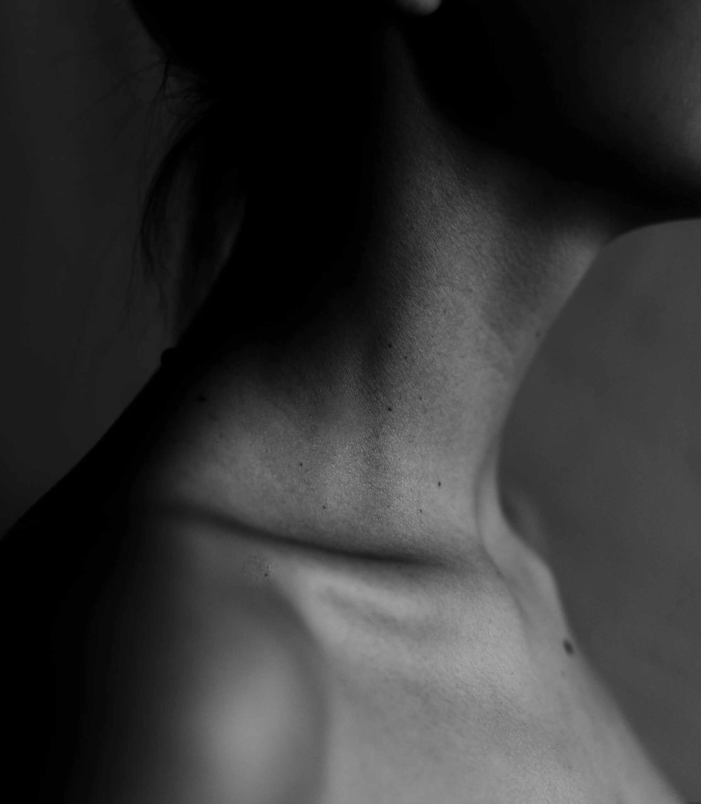Close-up black and white photo of a human face, partially visible, with focus on skin texture and neck and collar bone.