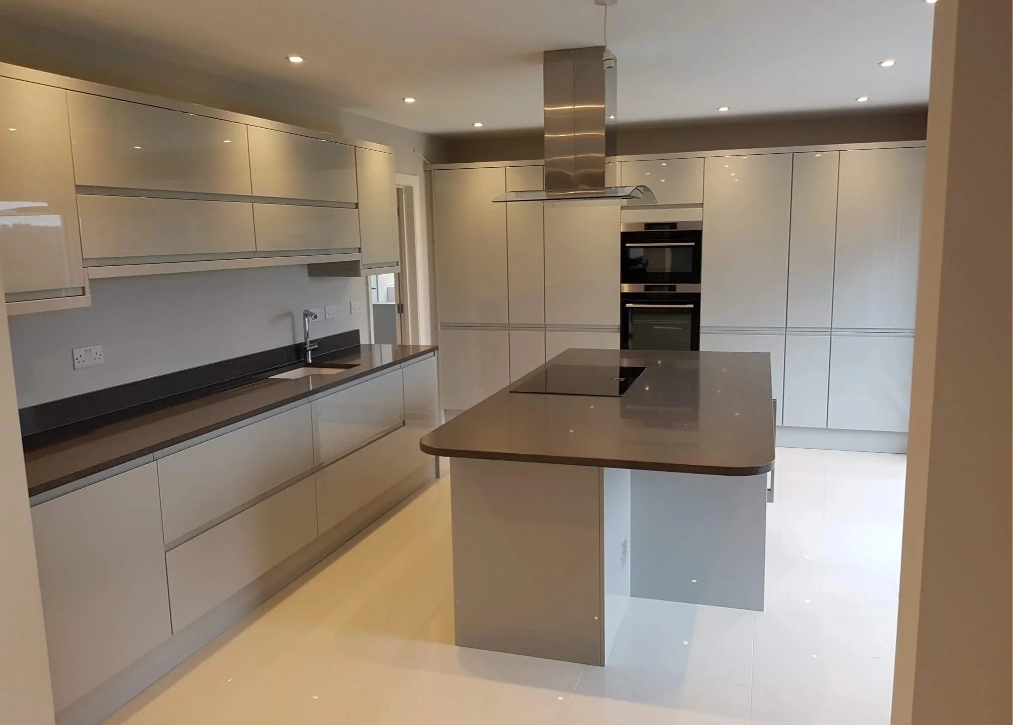 Modern kitchen with beige cabinets, black countertops, built-in double oven, stainless steel range hood, and a kitchen island.
