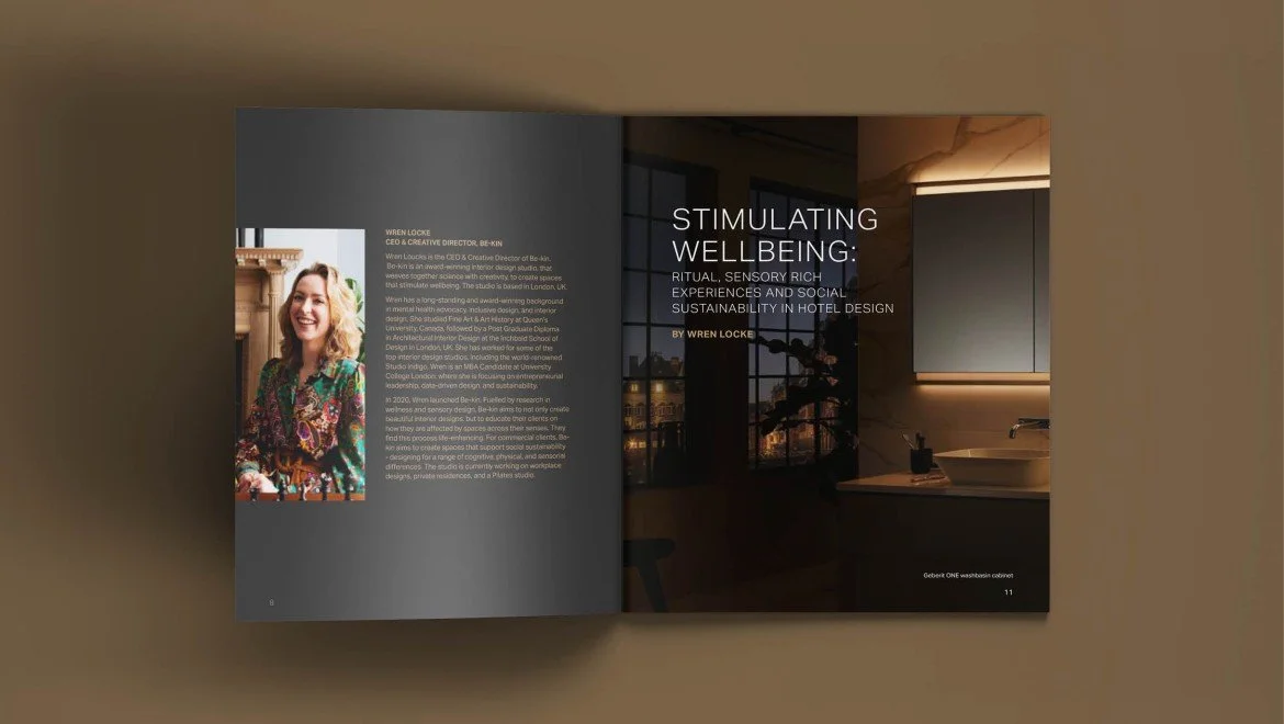 Open magazine with an article titled 'Stimulating Wellbeing: Ritual, Sensory Rich Experiences and Social Sustainability in Hotel Design' by Wren Locke, featuring a woman smiling in colorful attire on the left page and a modern interior with large windows and a sink on the right page.