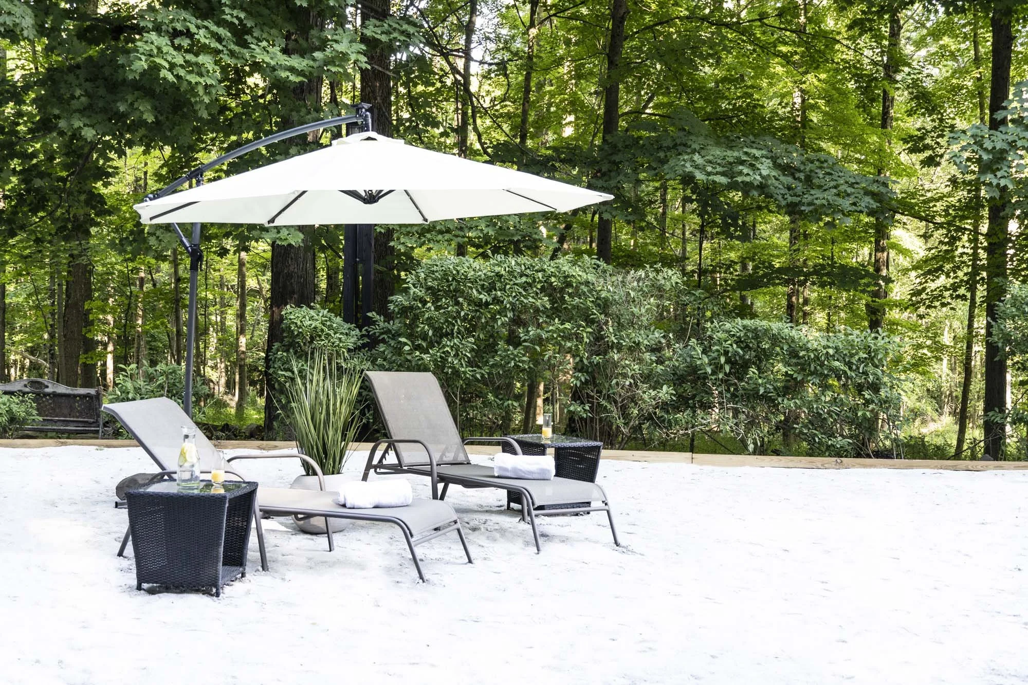 Outdoor pool area with poolside chairs and umbrellas, surrounded by lush green trees.