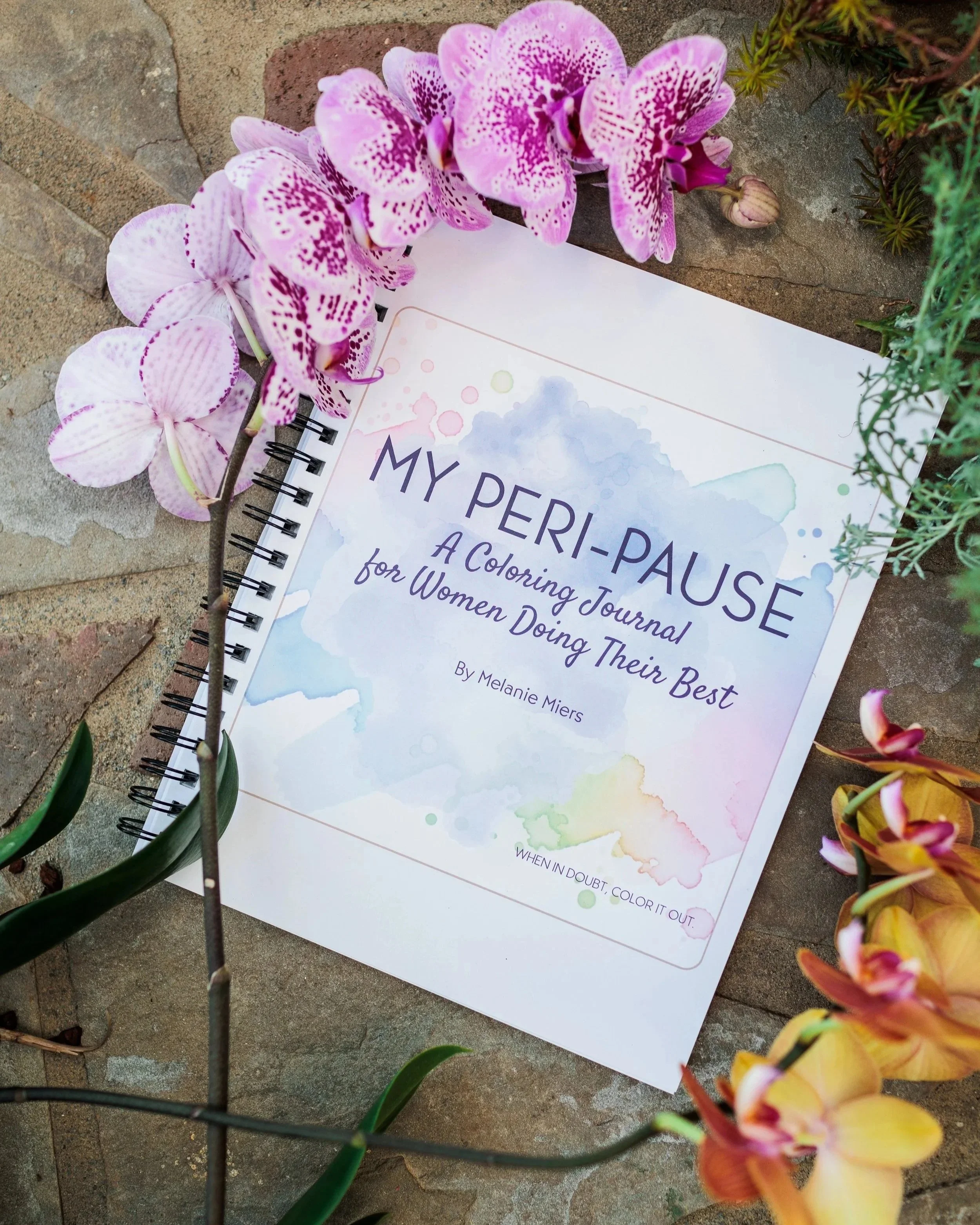 A coloring journal titled 'My Peer-Pause' surrounded by pink and yellow orchids and green plants on a stone surface.
