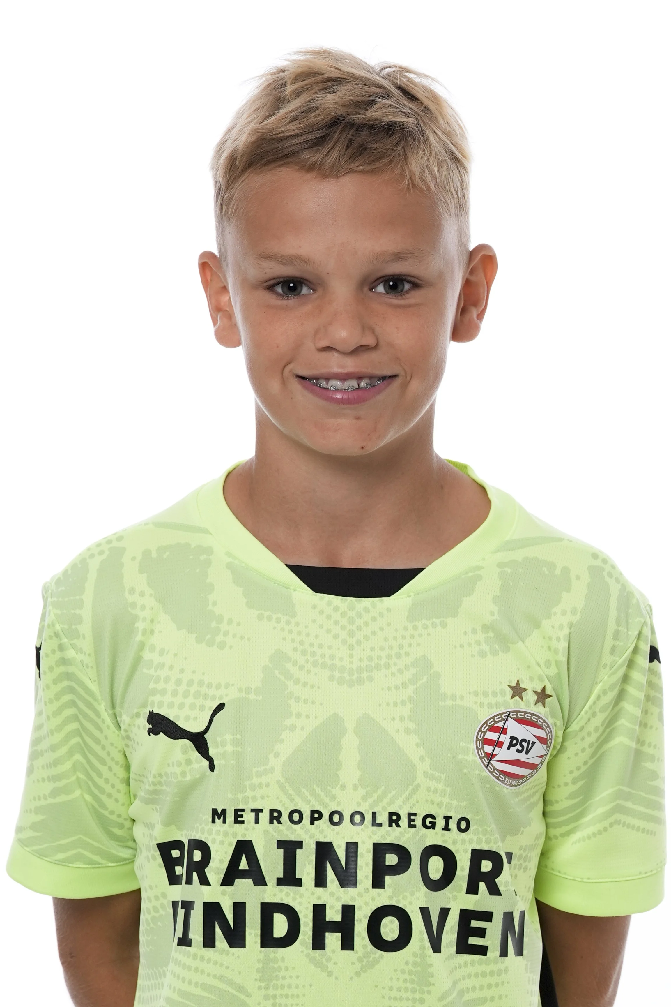 Jeugdige man in een lichtgroen PSV Eindhoven voetbalshirt met logo en sponsor, glimlachend, op een witte achtergrond.