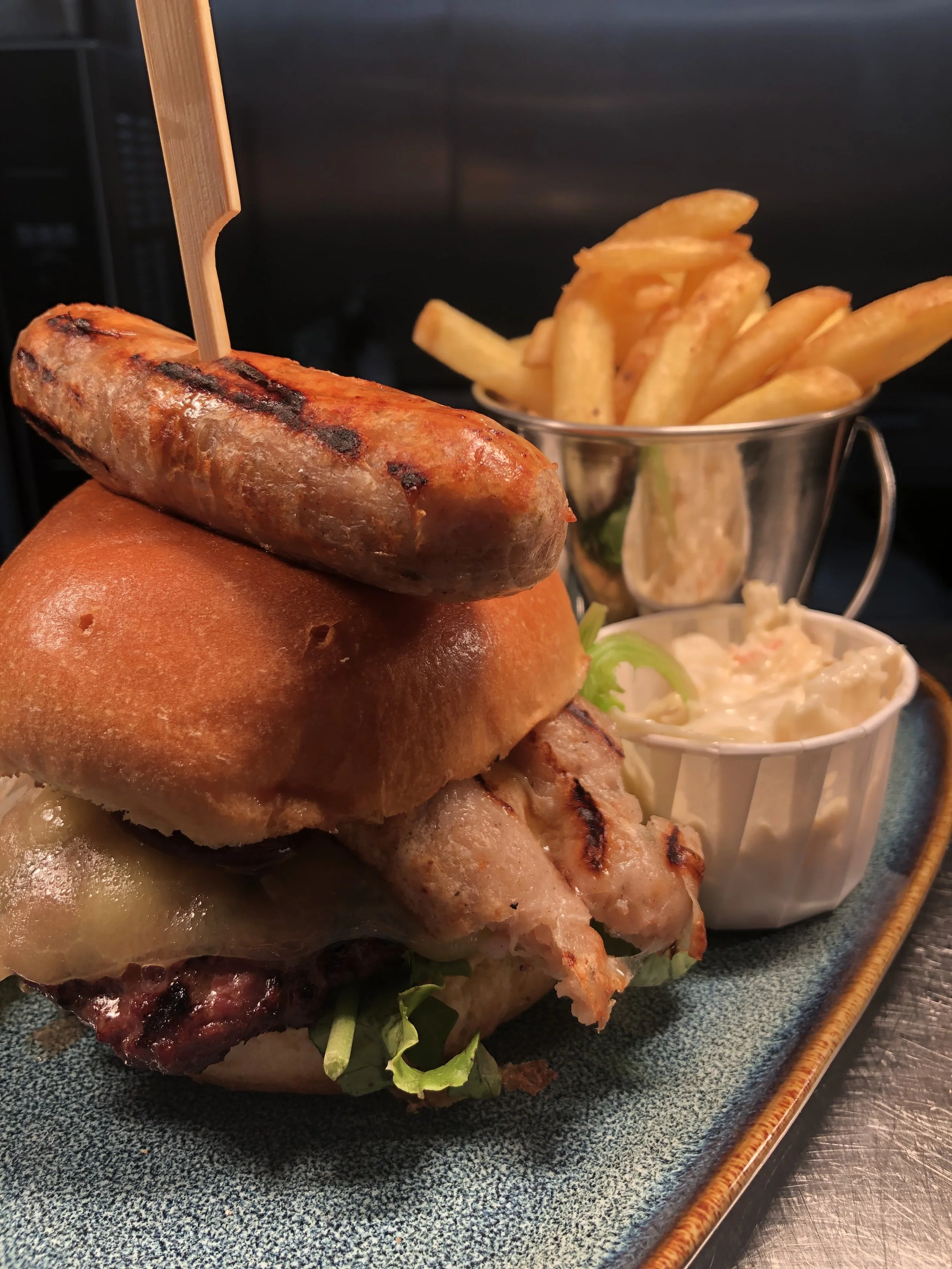 A plate of food featuring grilled sausage, fried chicken, French fries, coleslaw, and a bread roll.