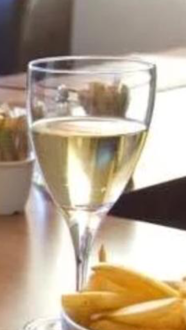 A glass of white wine on a table with some banana chips nearby.