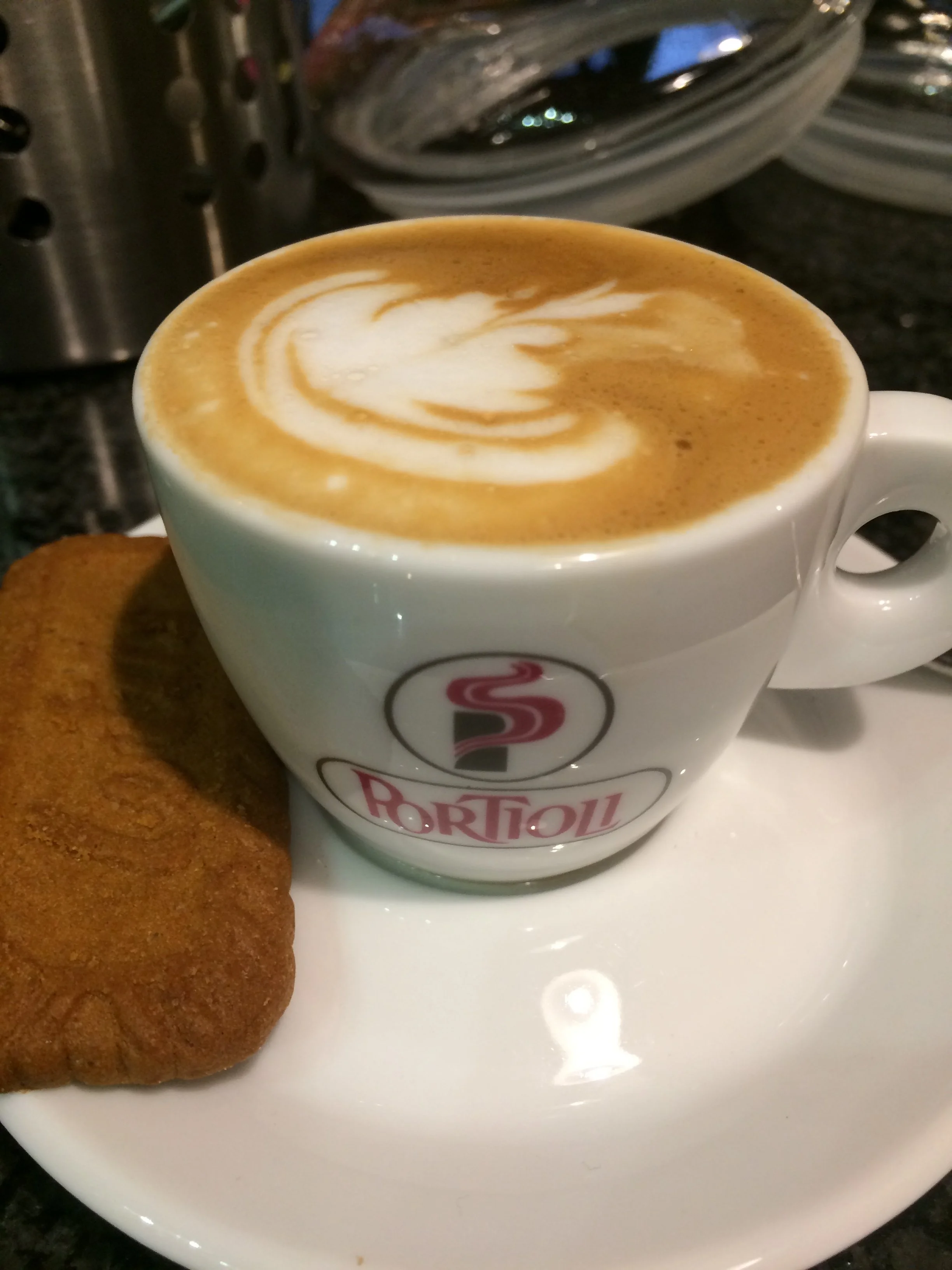 A cup of coffee with latte art in a white ceramic mug and a chocolate cookie on a white plate.