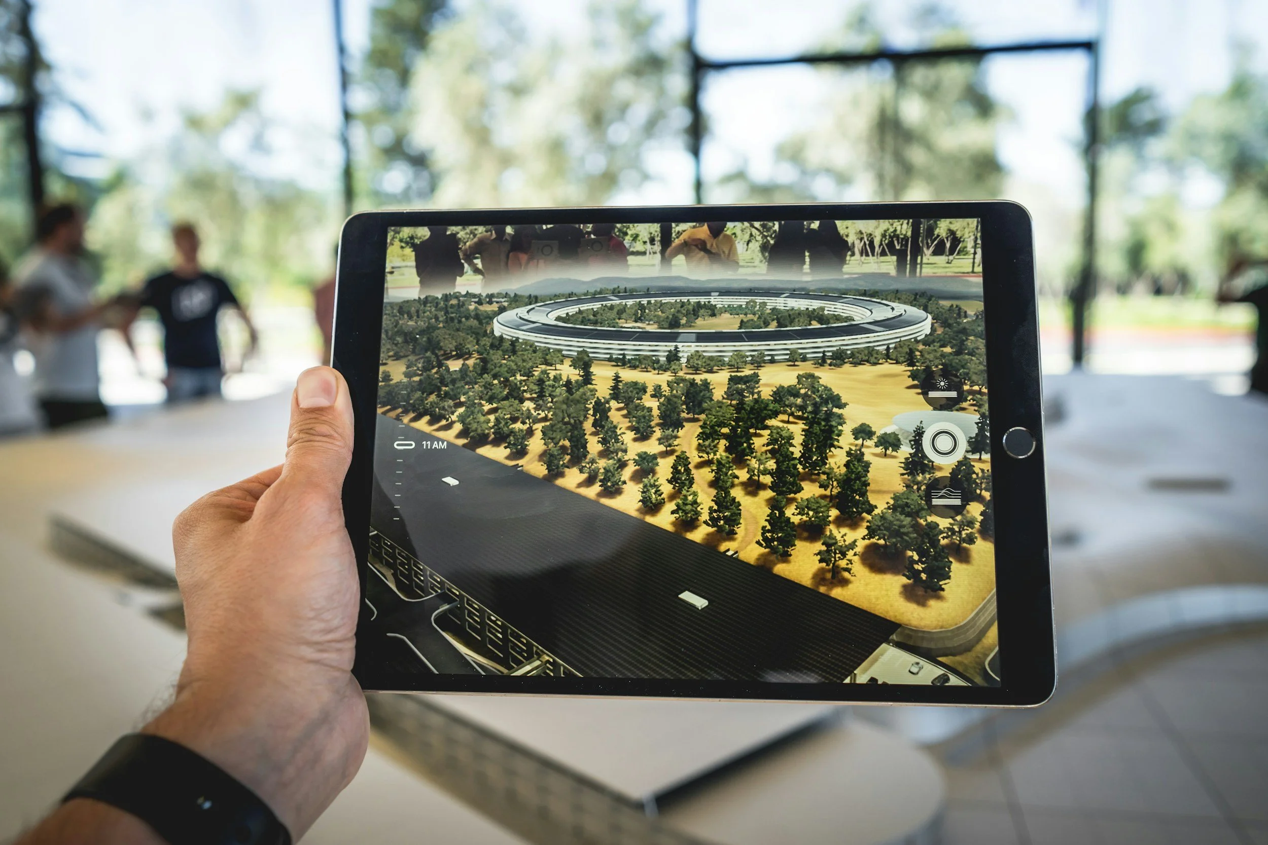 Person holding a tablet displaying a digital rendering of a circular building with trees, with three people observing in the background.