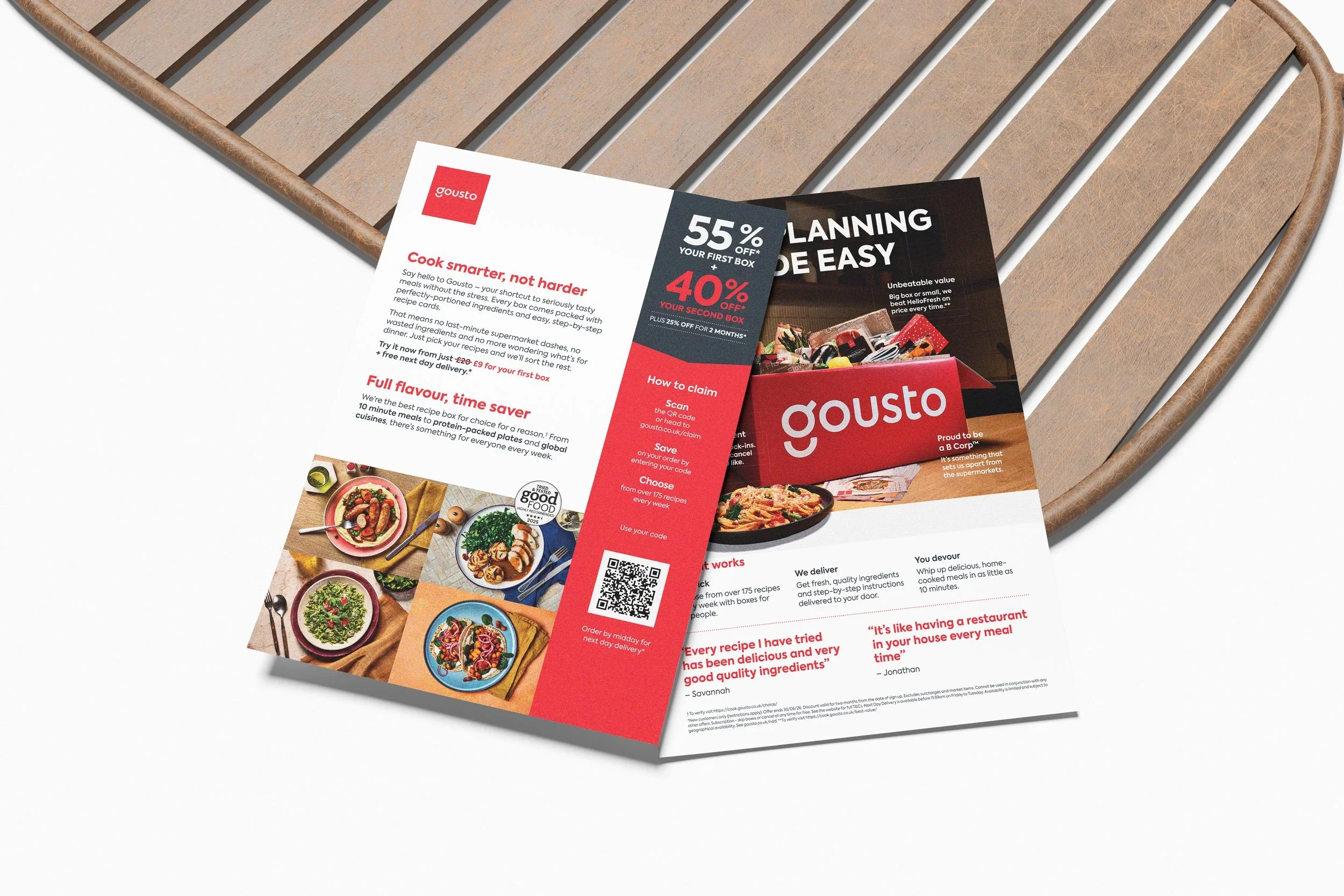 Two flyers for Gousto meal kit delivery service placed on a wooden tray. The flyers feature images of various cooked dishes, text about discounts, and instructions on how to claim discounts.