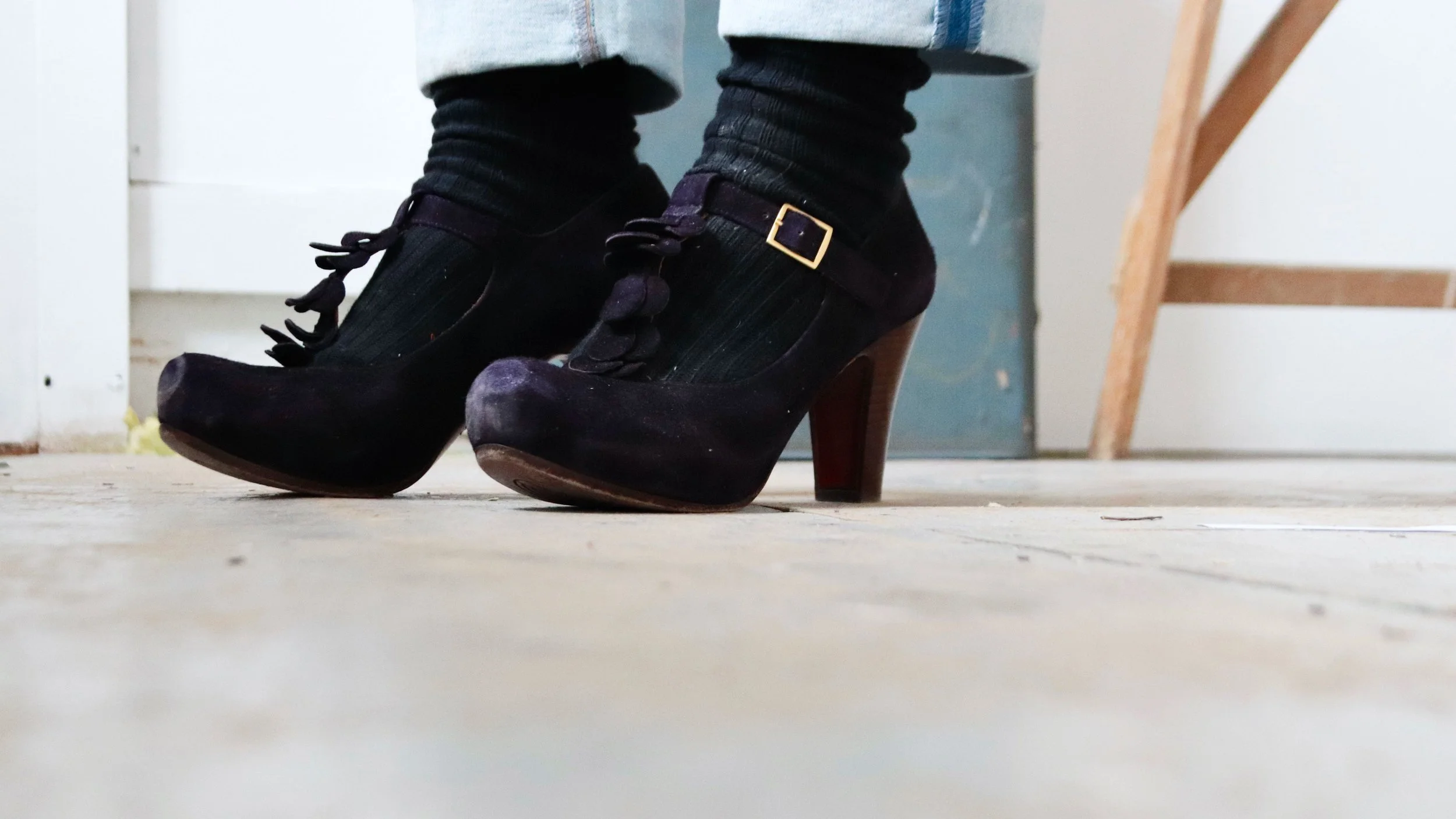 Close-up of black heeled shoes with buckles and tassels, worn with black socks 