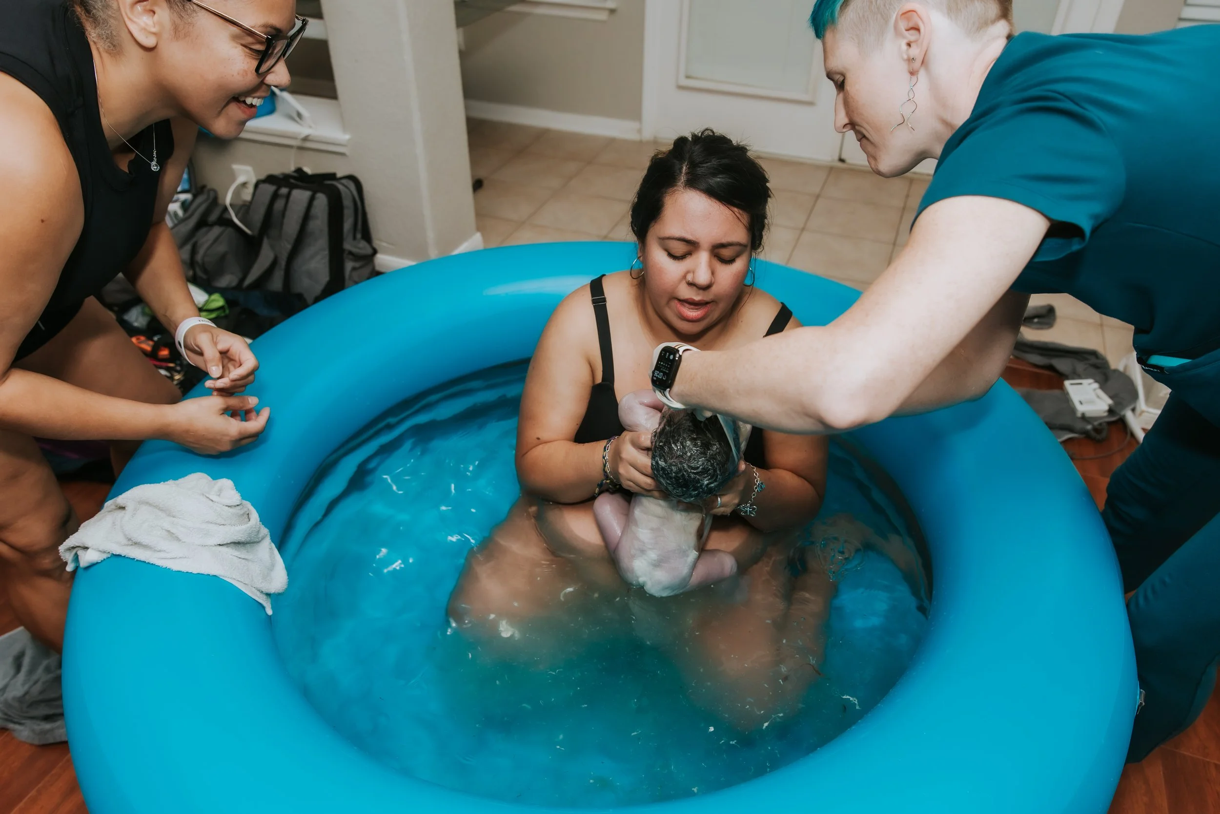 Person being baptized in a small blue pool surrounded by two other individuals during a religious ceremony.
