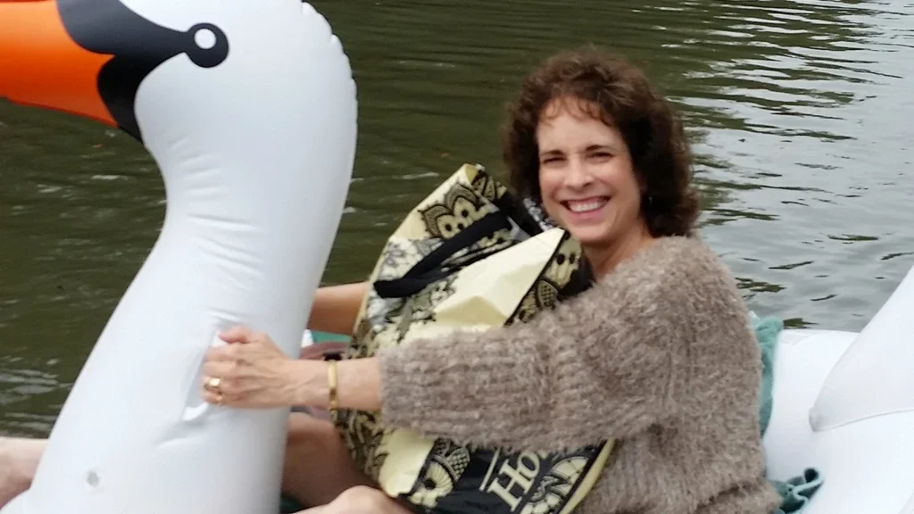 Woman smiling on a boat holding onto a large inflatable swan in a body of water.