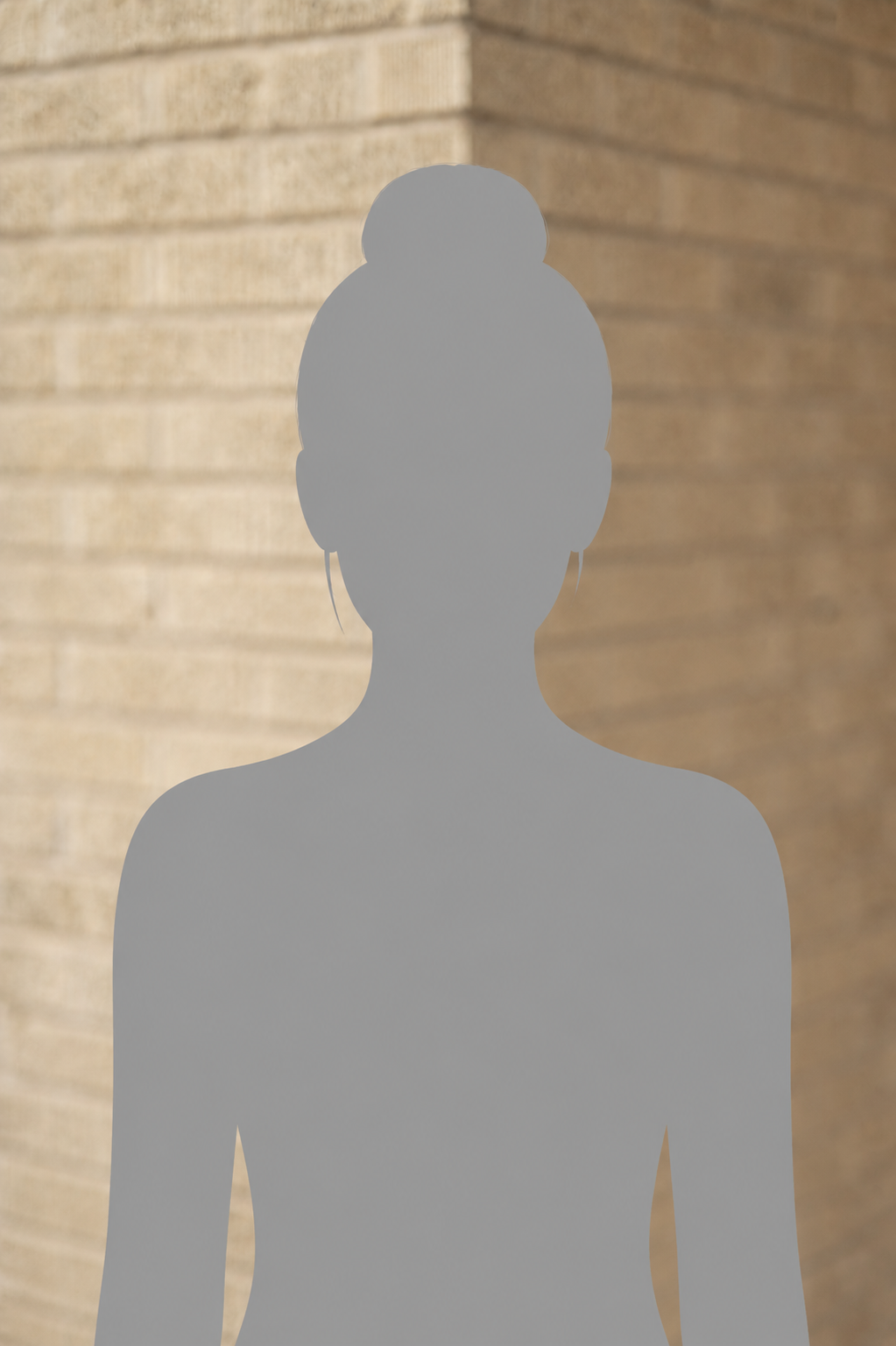 Silhouette of a person with their hair in a bun, standing against a tan brick wall.