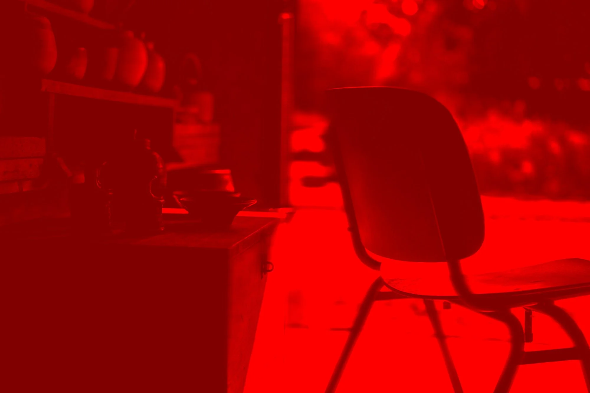 Ein Stuhl vor einem roten, verrauschten Hintergrund, kaum erkennbare Gegenstände auf einem Tisch, eine Dose und eine Tasse.
