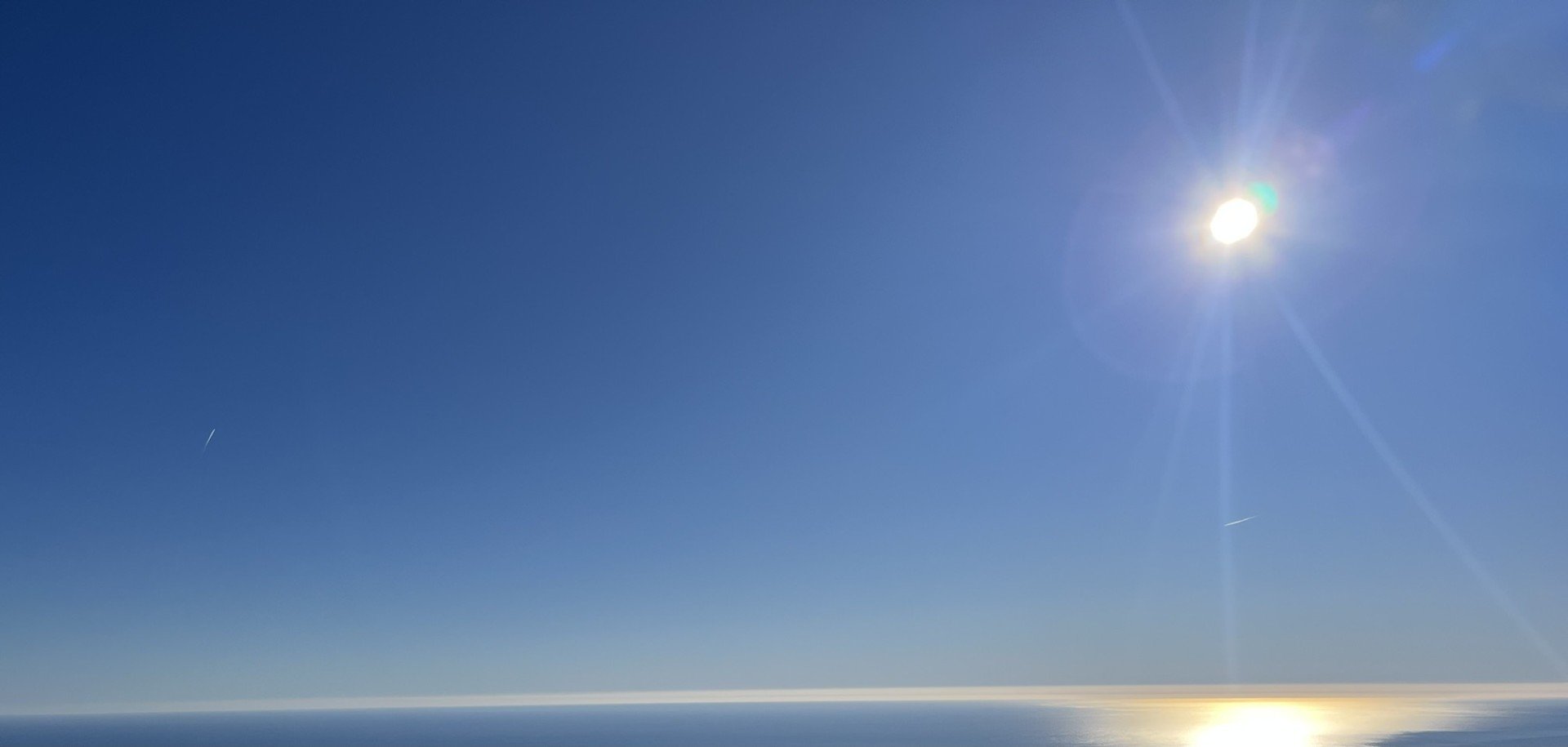Ciel clair avec le soleil brillant à Sallanches , reflet de la lumière sur l'océan en dessous, deux traînées d'avion visibles.
