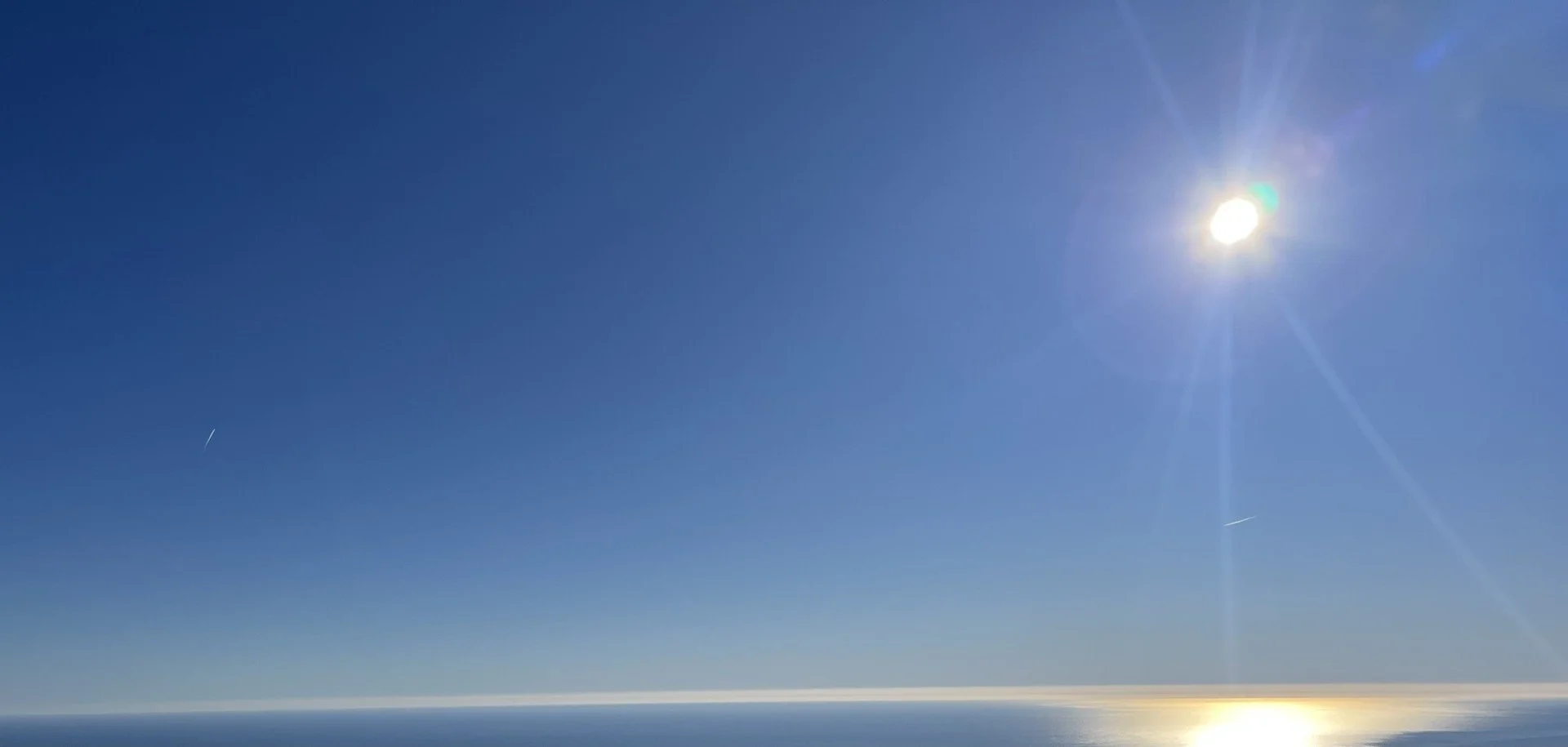 Ciel clair avec le soleil brillant, mer calme en dessous, deux traînées d'avion dans le ciel, au dessus de Sallanches