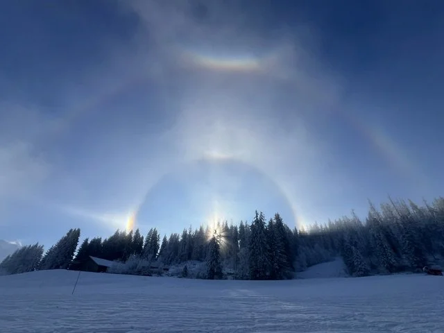 Arc-en-ciel de halo lumineux dans un ciel bleu au-dessus d'une forêt enneigée, à Chamonix
