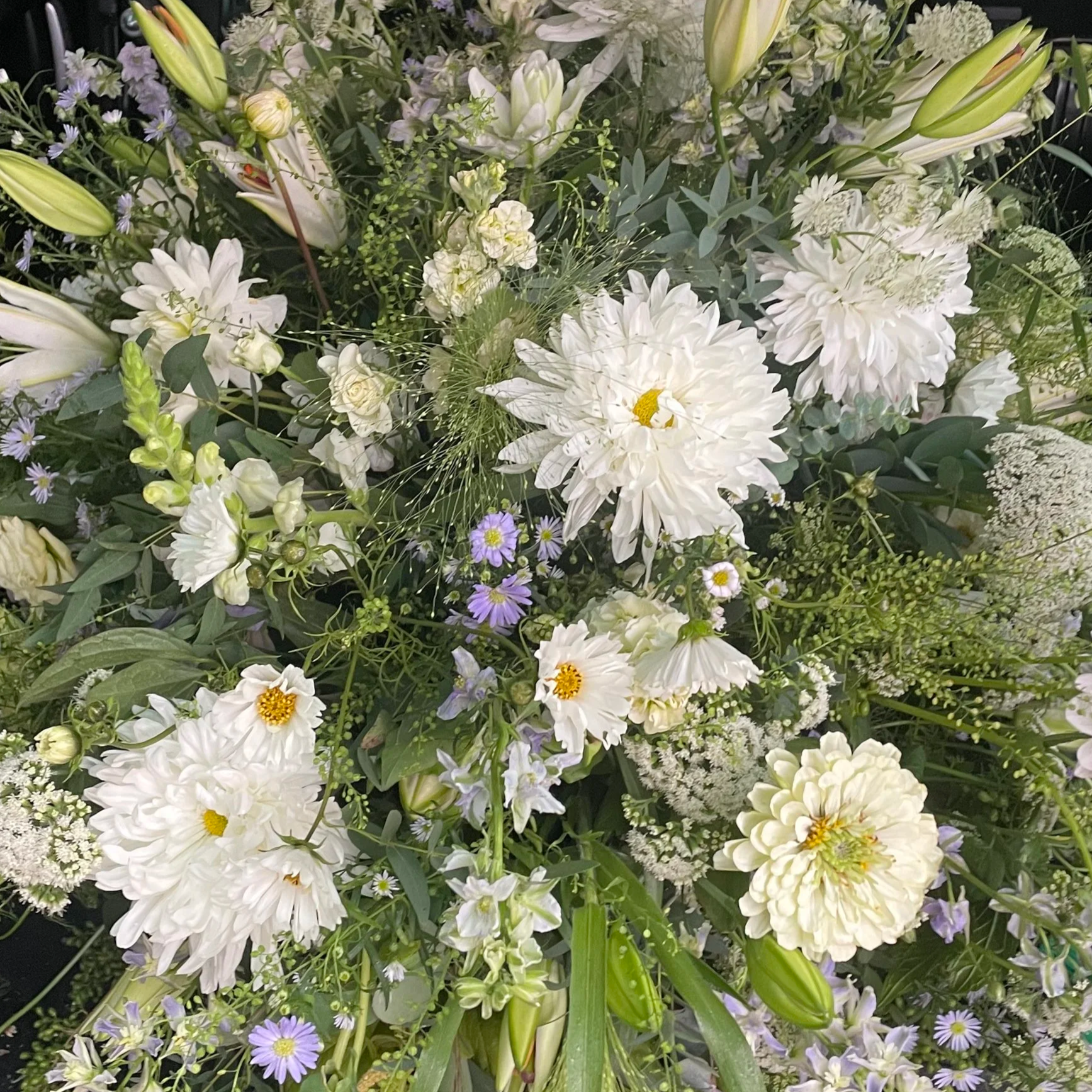 A bouquet of white and purple flowers, including lilies, dahlias, and daisies, arranged with green foliage.