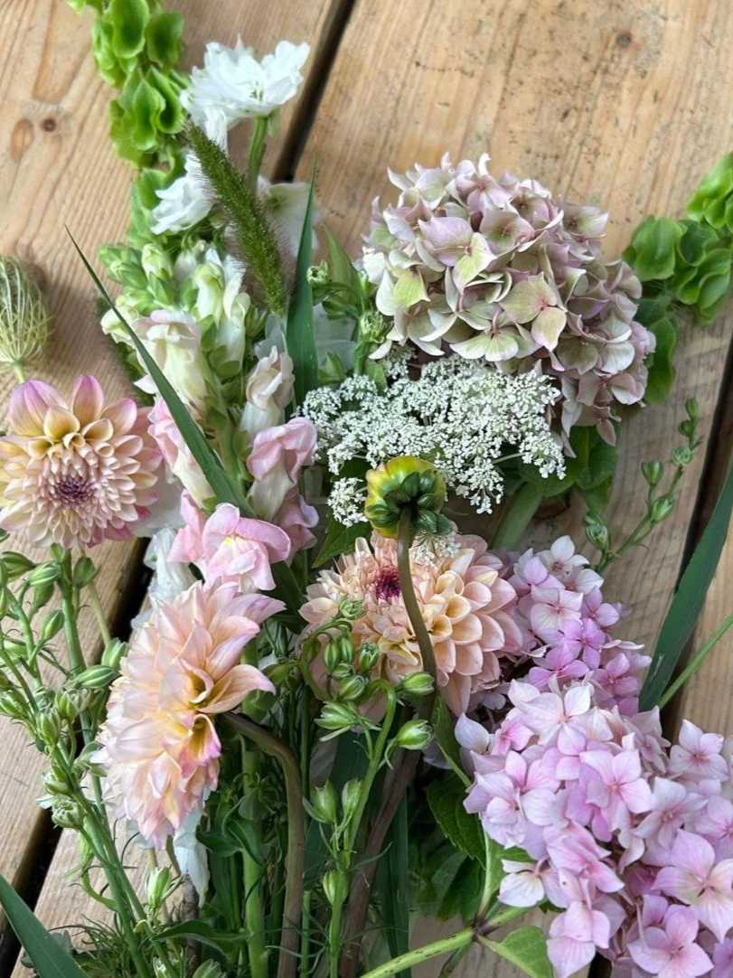 A variety of colorful flowers, including pink and red roses, white daisies, purple and green buds, and dried grasses.