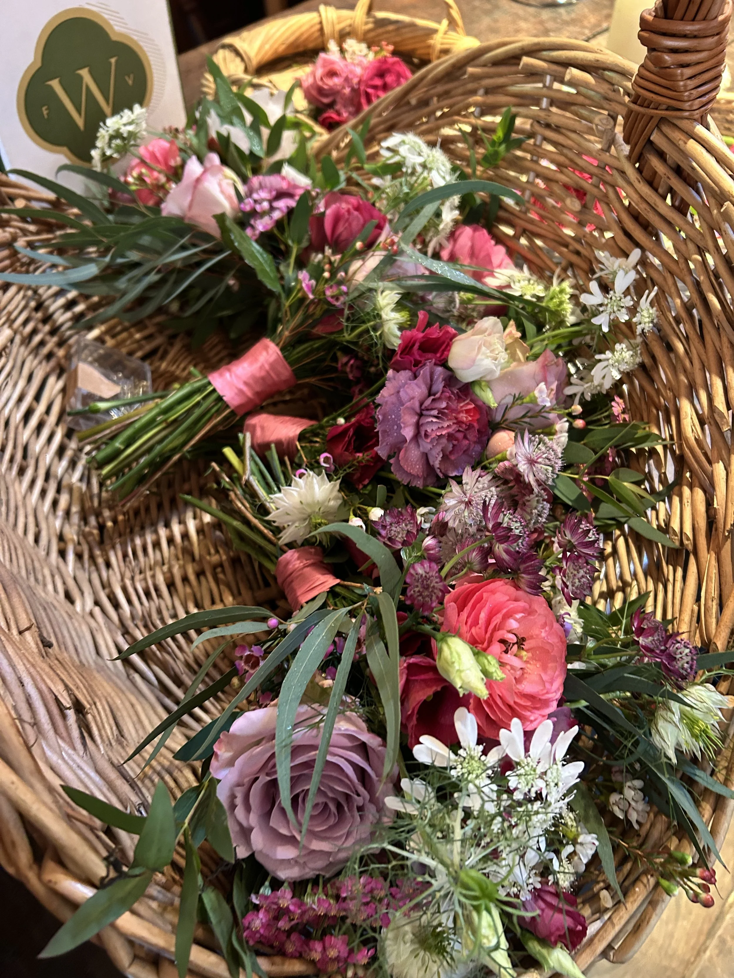 Colorful bouquet of pink, purple, white, and green flowers in a wicker basket.