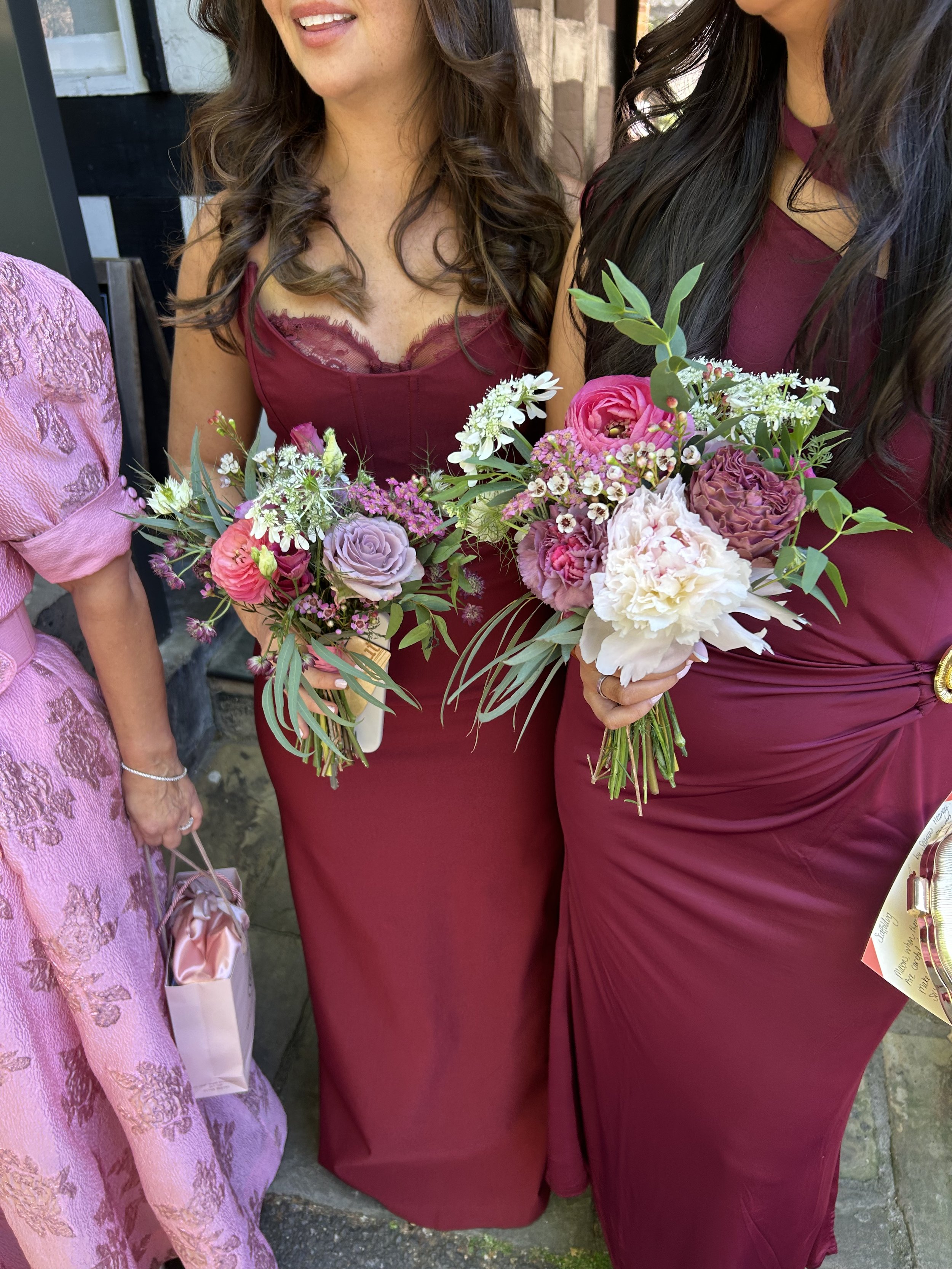 Two women wearing burgundy dresses holding bouquets of flowers, standing together.