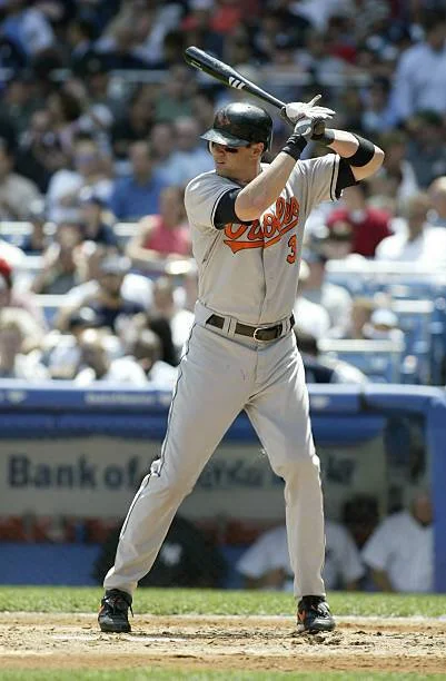 A baseball player in a white uniform with red and black accents, standing at home plate with a bat, ready to hit during a game at a stadium.