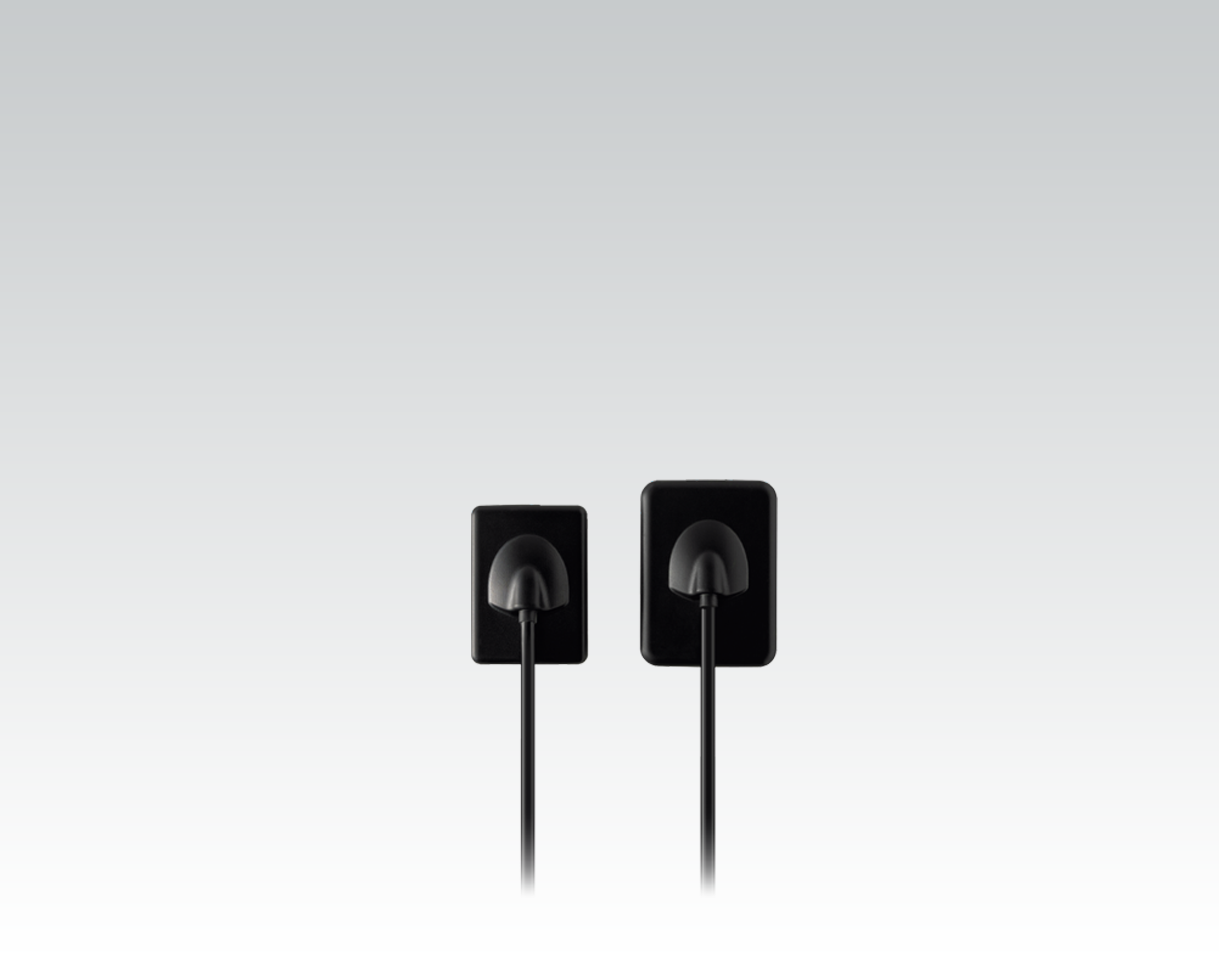 Two black electrical charging cords plugged into black wall outlets on a light gray wall.