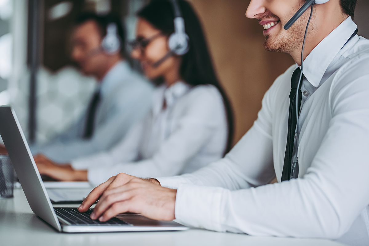 Customer service representatives wearing headsets working on laptops in an office.