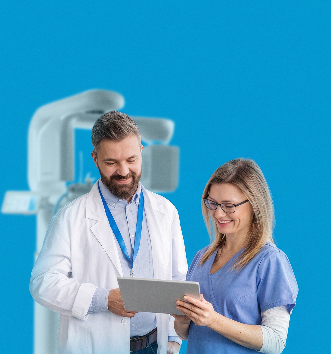 A male doctor and a female nurse looking at a tablet screen with a medical imaging machine in the background.