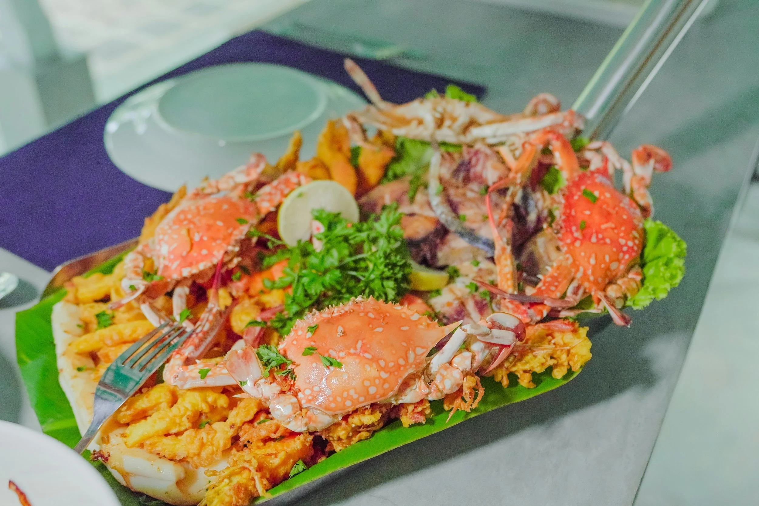 Seafood platter with crab legs, lobster tail, lemon wedge, and garnishes on a green leaf in a boat-shaped dish.