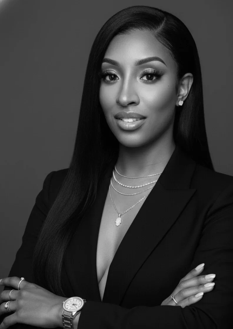 Black and white portrait of a confident woman with long straight hair, wearing a blazer, jewelry, and a watch, with arms crossed.