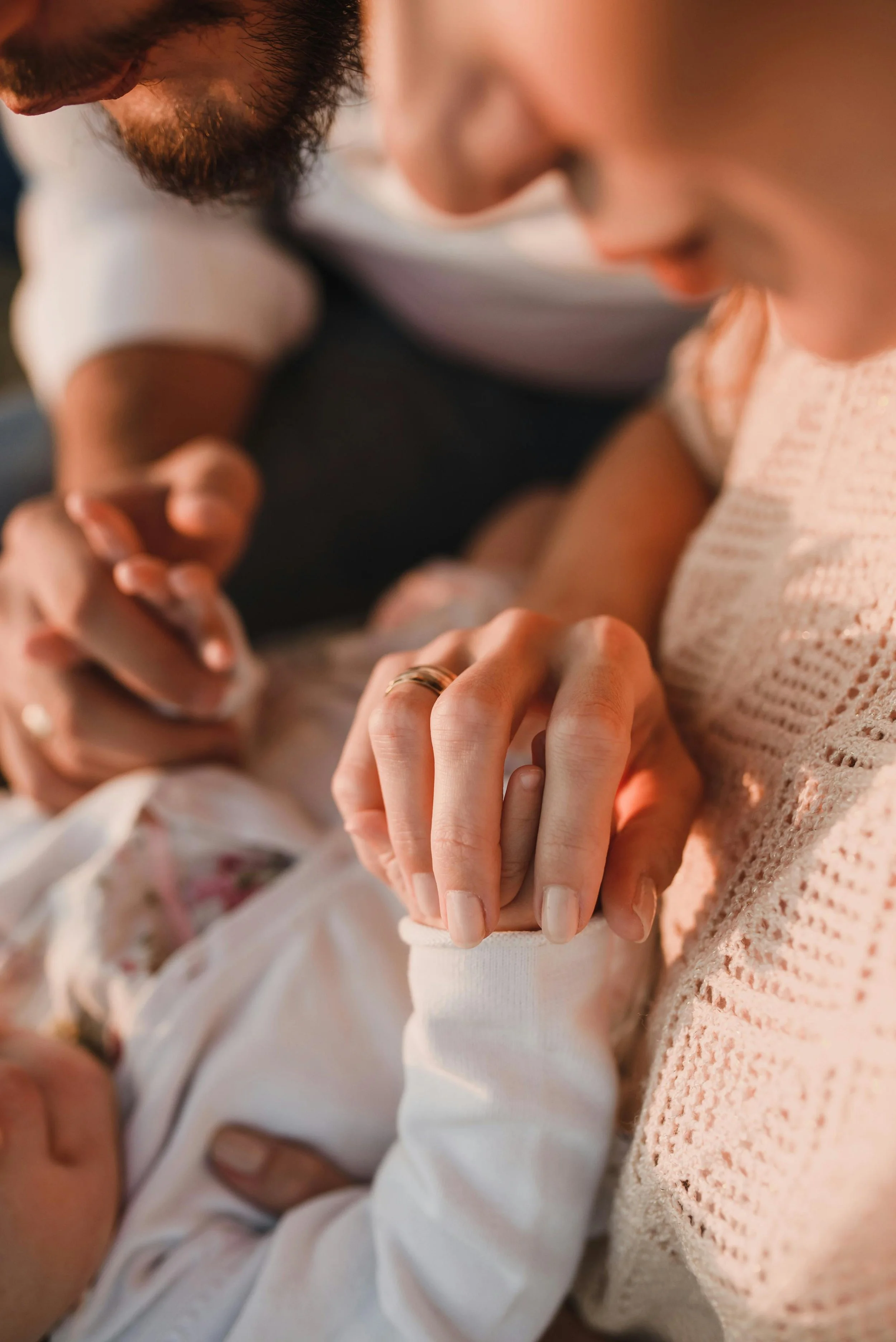 Close-up of a parent and a child's hands holding each other, with the parent's face partially visible and the child's face blurred in the background.