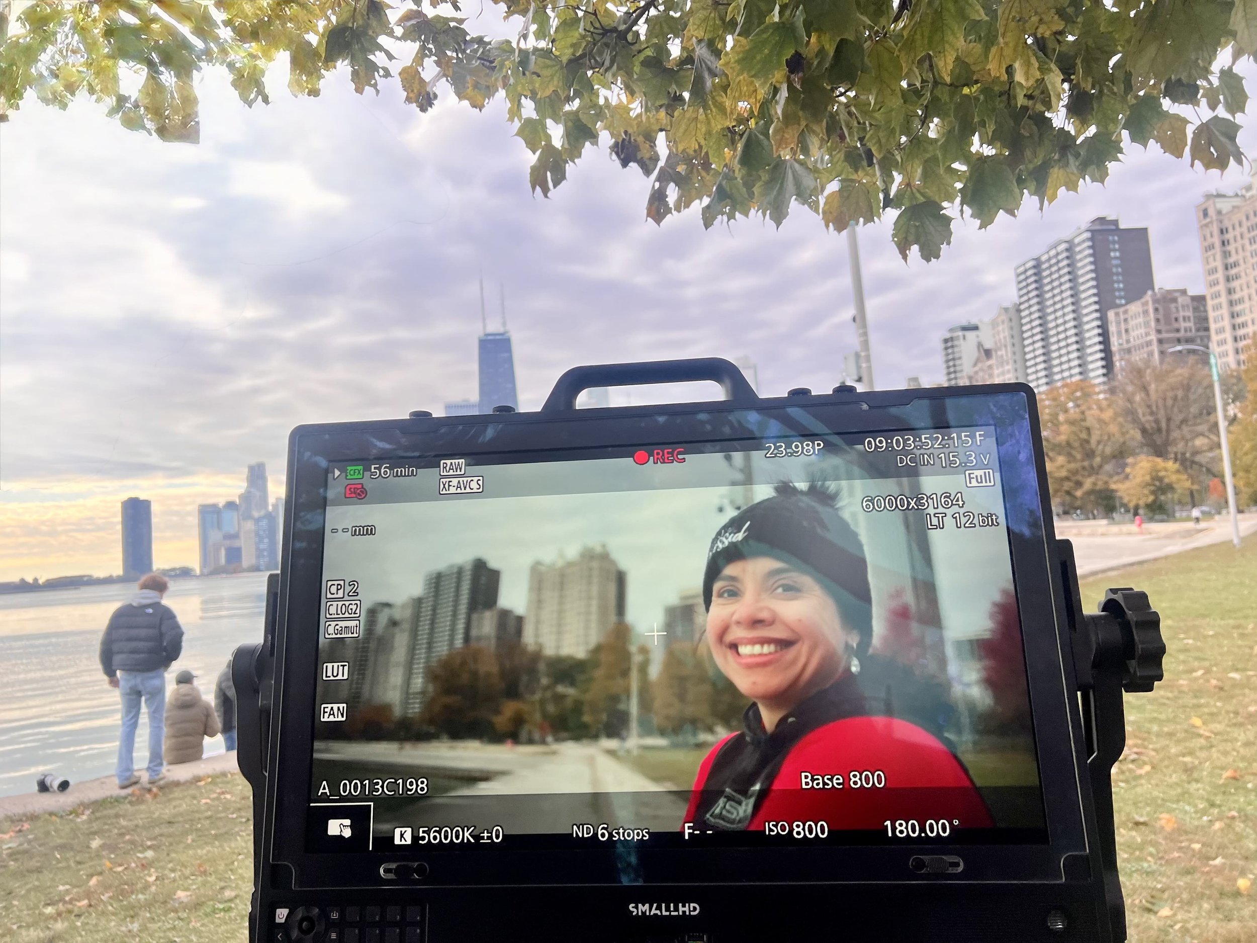 A production monitor on set showing a smiling woman on camera, with a city skyline behind