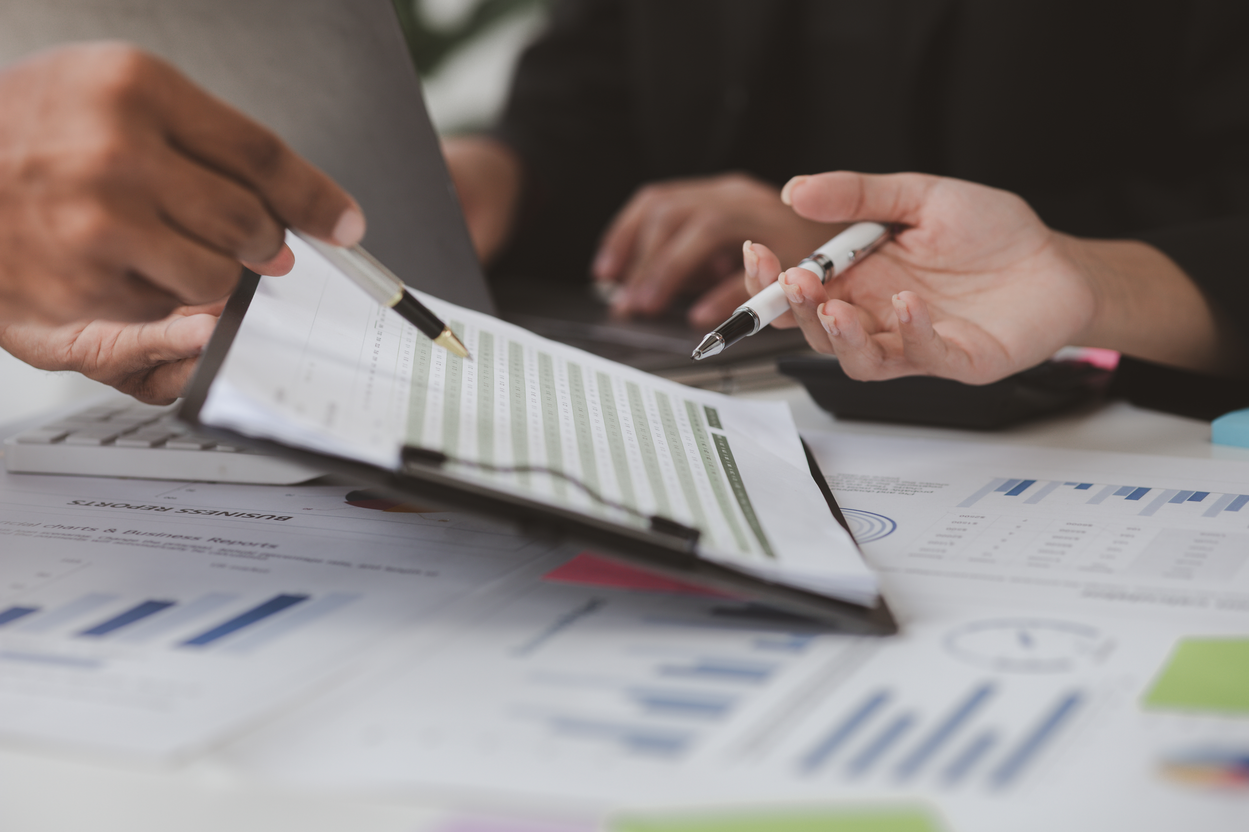 Close-up of two hands exchanging pens over printed documents and charts.
