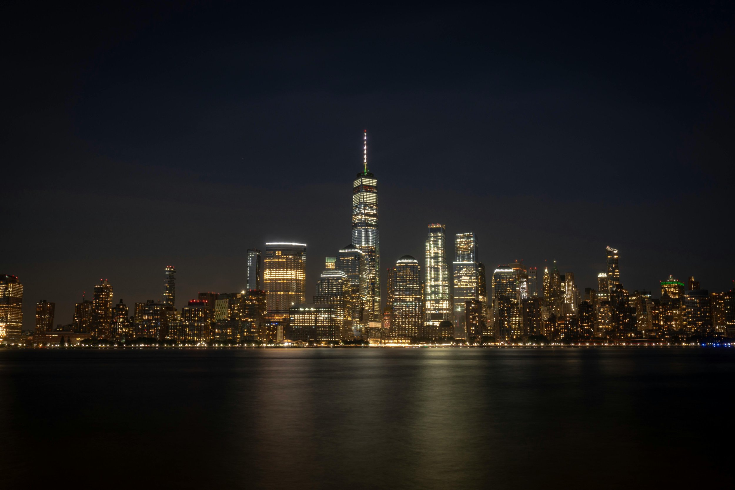Night view of New York City skyline with illuminated buildings and One World Trade Center.