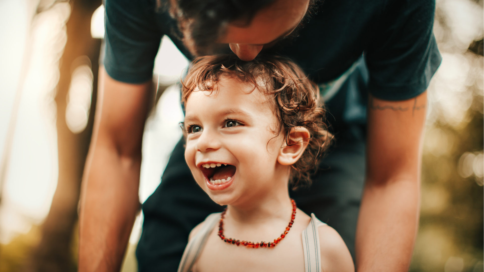 Smiling child with his father in the background reaching down to hug him