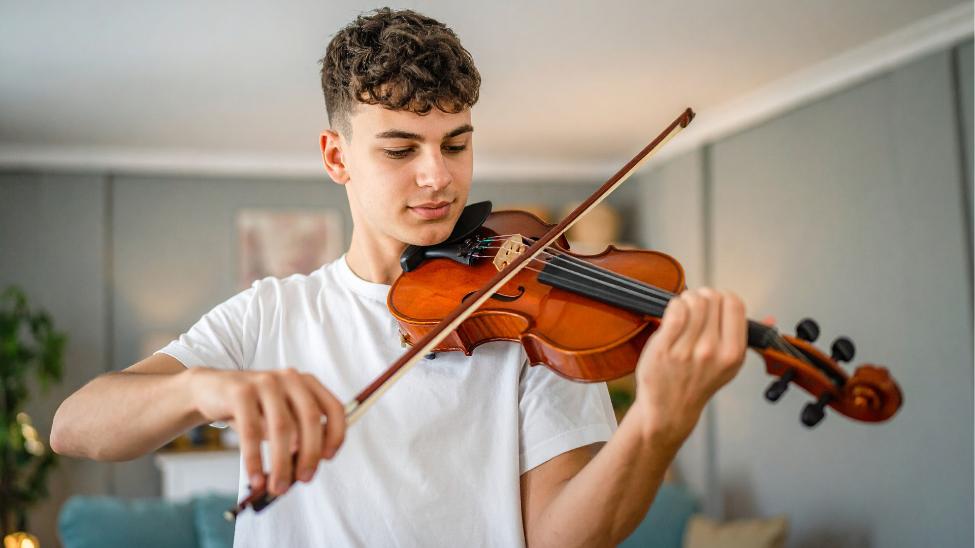 Young man playing the violin indoors, wearing a white t-shirt.