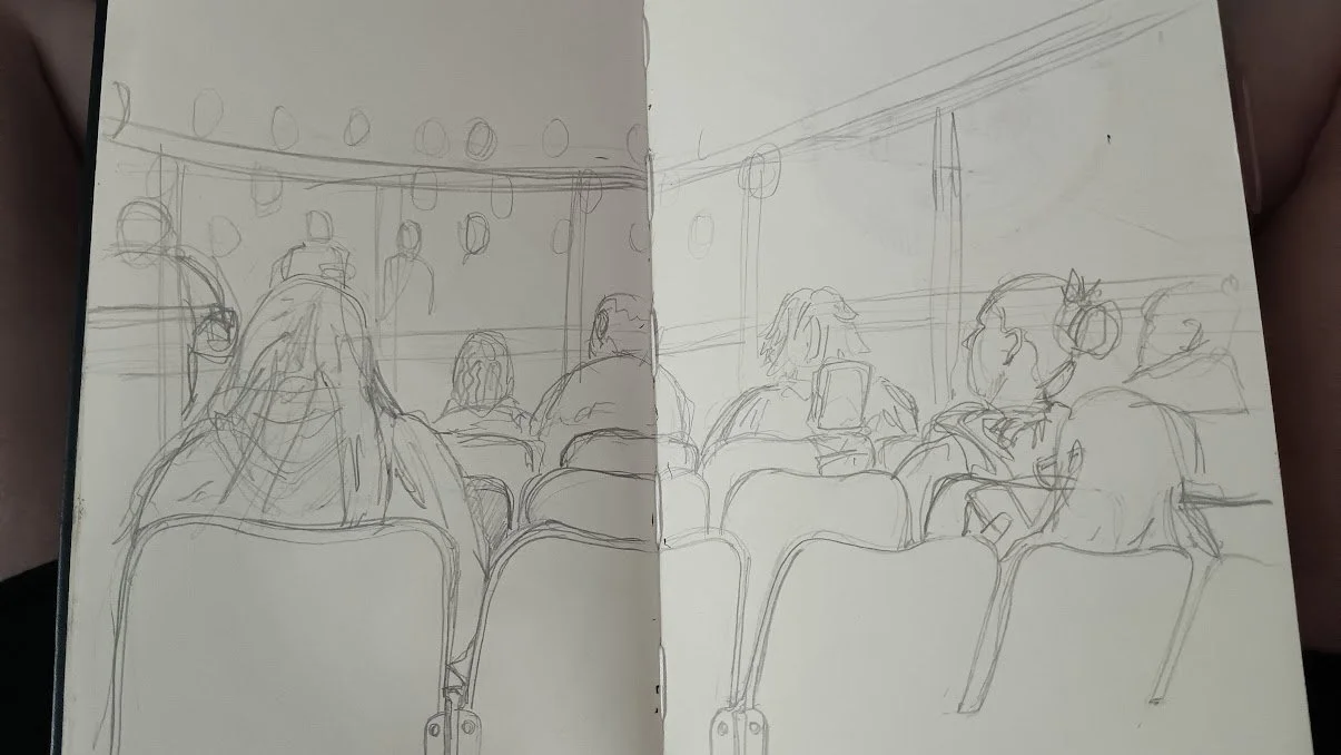 A sketch of people sitting in chairs in an auditorium or conference room, facing a stage or screen at the front.