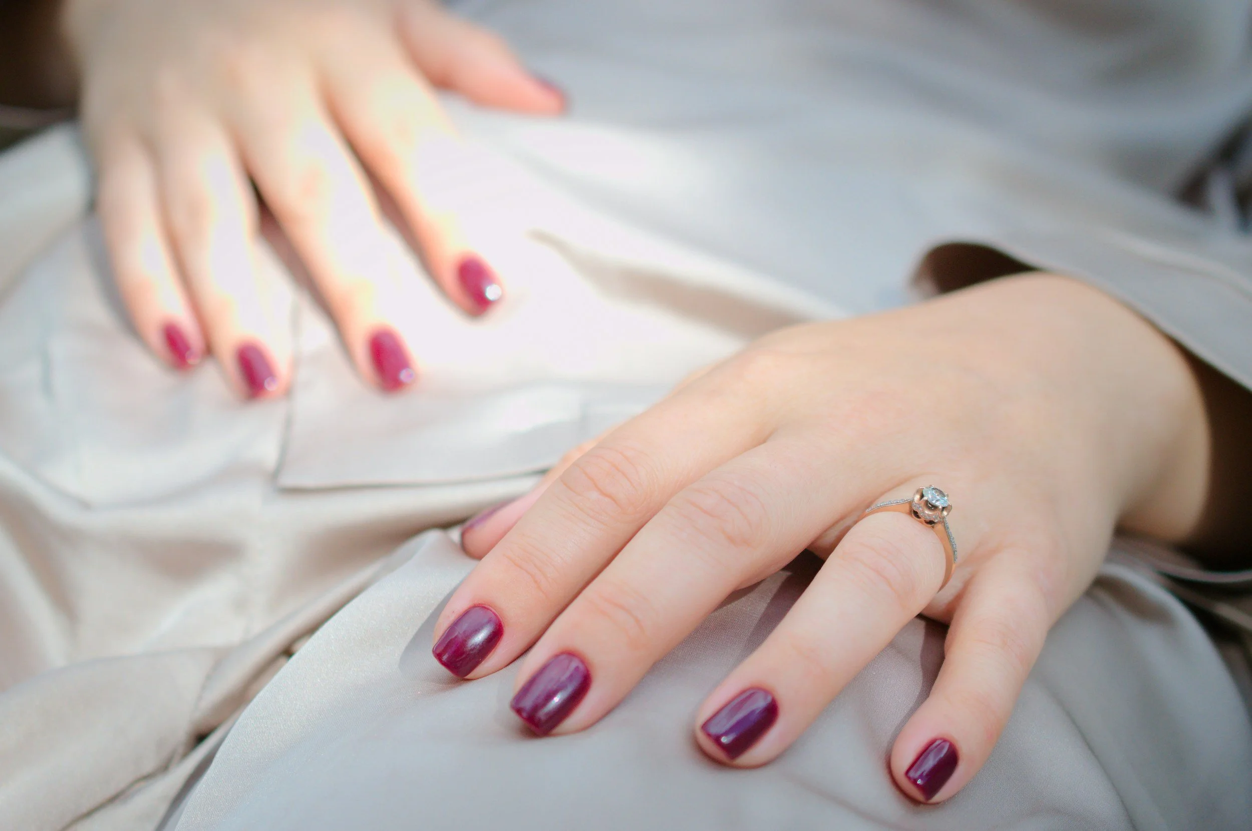 Close-up of a hand with an elegant deep red manicure and a diamond ring, resting on satin fabricCompact powder makeup and mirror in soft rose tones, from LeLab Bare Beauty's collection
