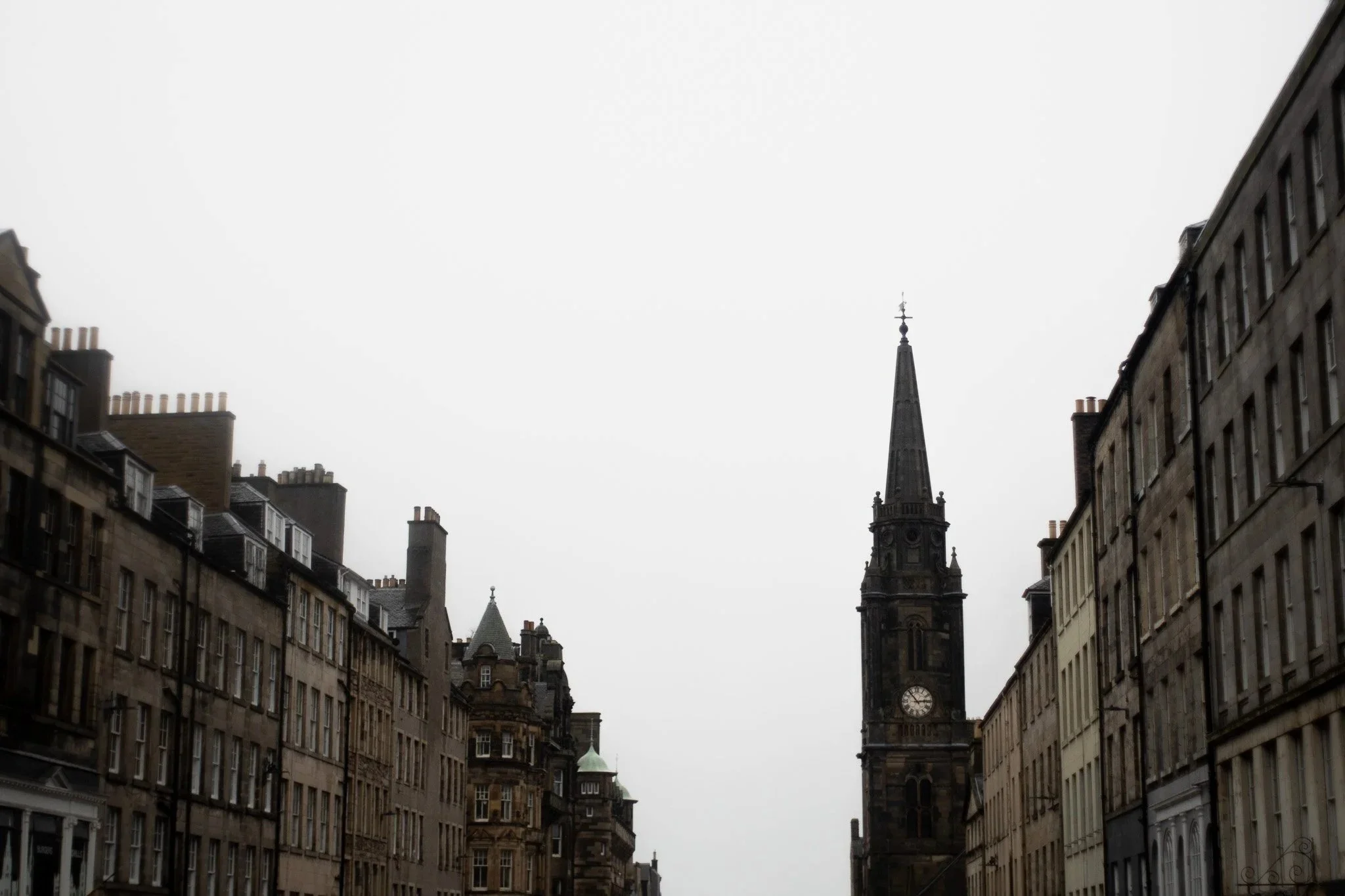 View of old European-style buildings lining a street with a church steeple in the background under a cloudy sky.