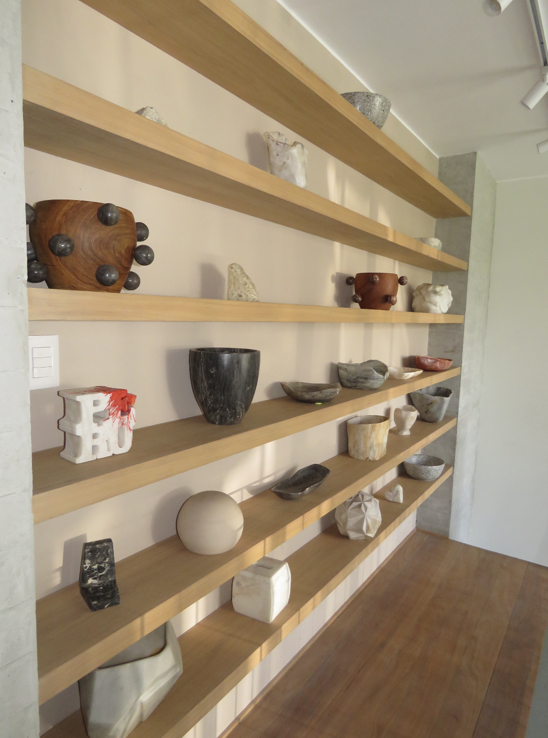 Wooden shelves displaying various pottery and stone art pieces inside a modern room.